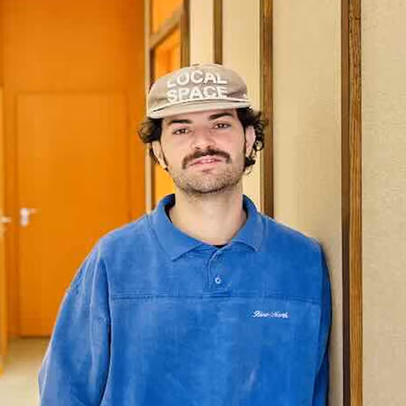 Portrait d'un homme aux cheveux courts bruns avec un léger sourire, en arrière-plan un salon lumineux avec des plantes et du mobilier moderne.