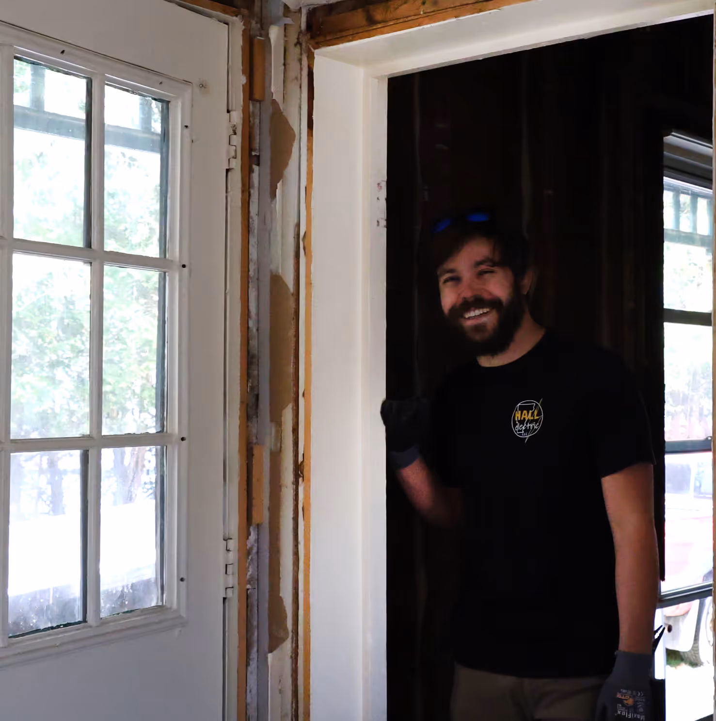 Smiling man standing in a doorway near a windowed door in a partially renovated room.