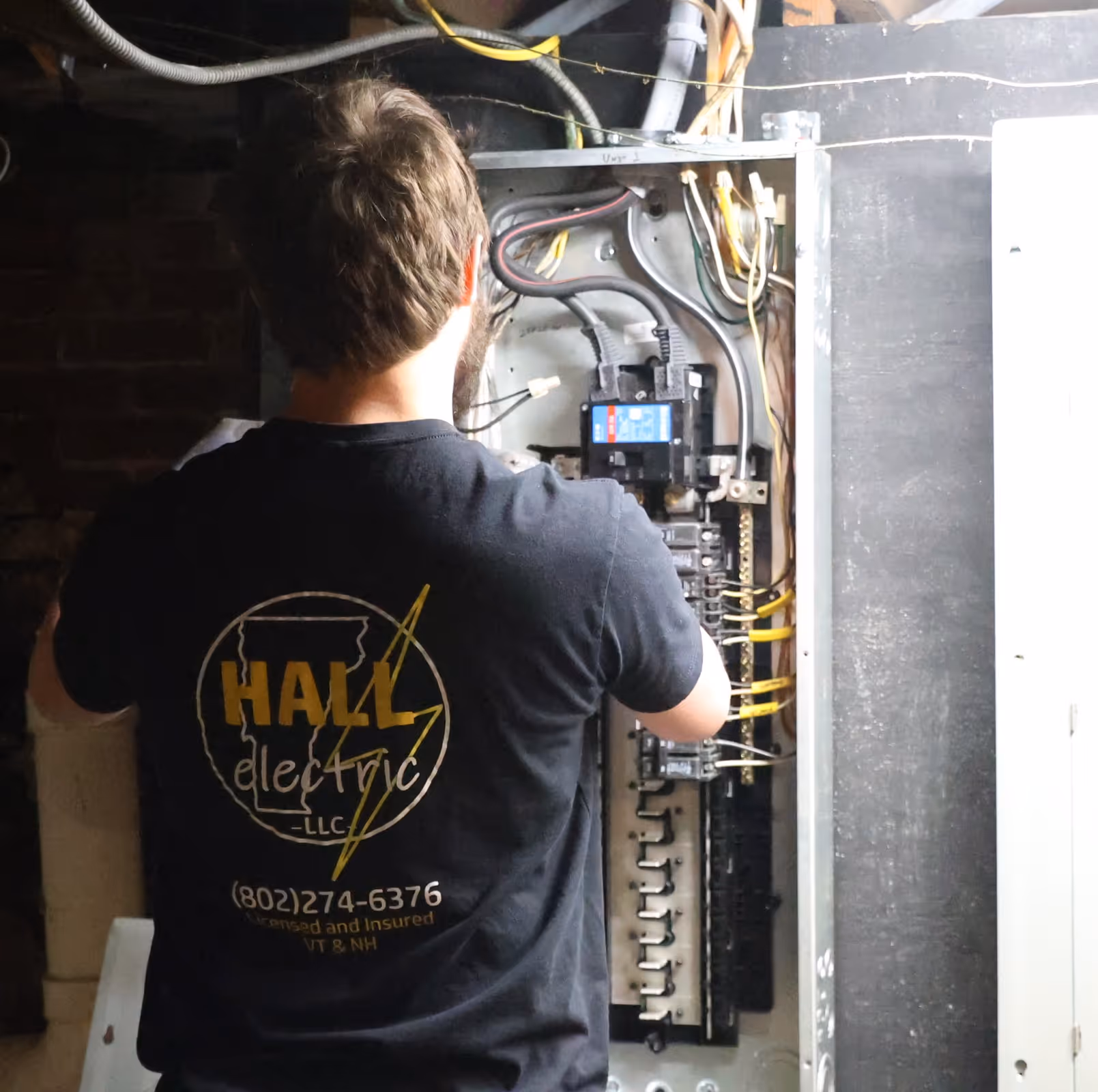 Electrician working on an open electrical panel with wiring and circuit breakers.