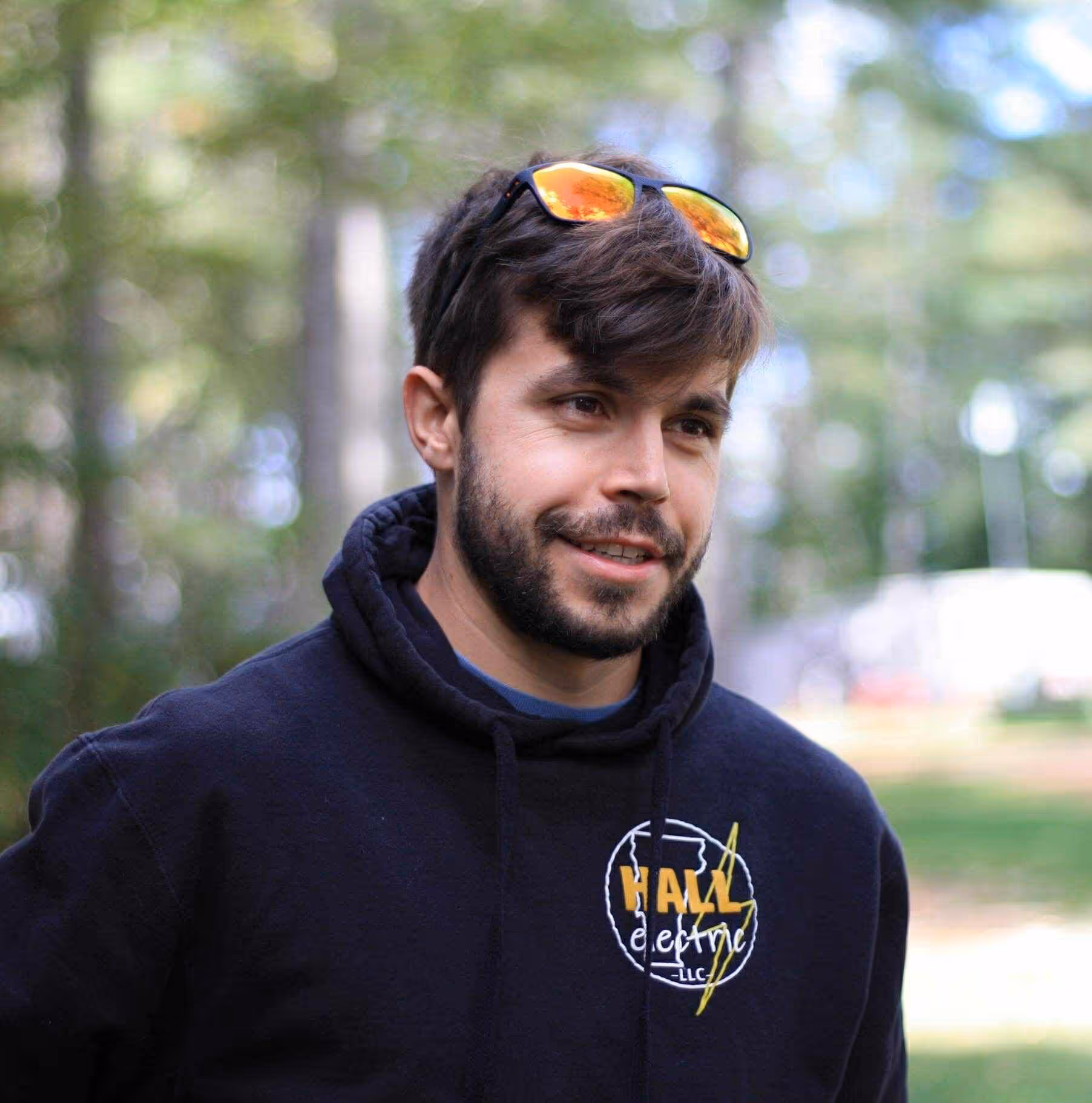 Young man with beard wearing sunglasses on head and Hall Electric hoodie outdoors