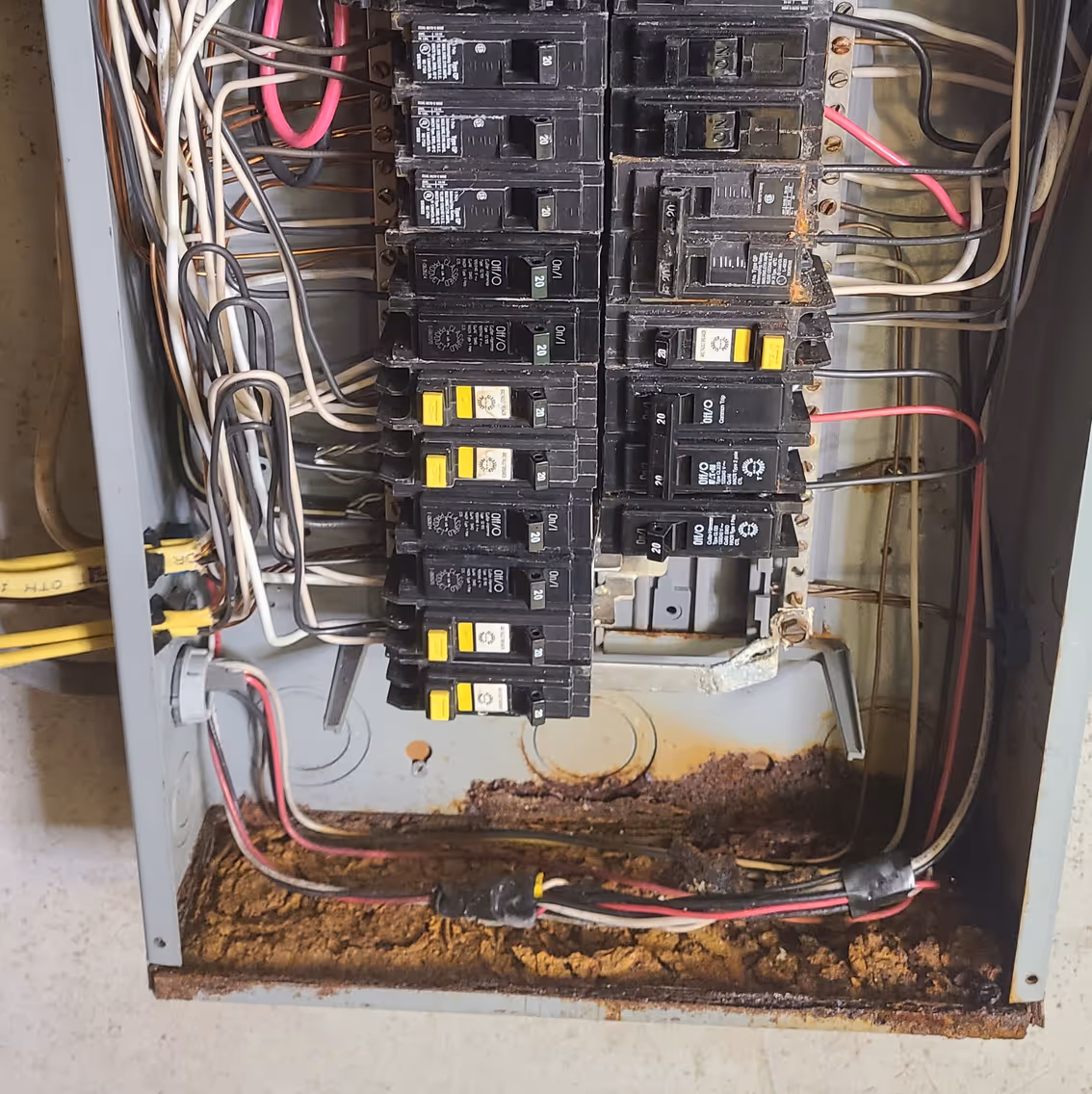 Water-damaged electrical breaker panel with multiple circuit breakers and visible rusty corrosion at the bottom.