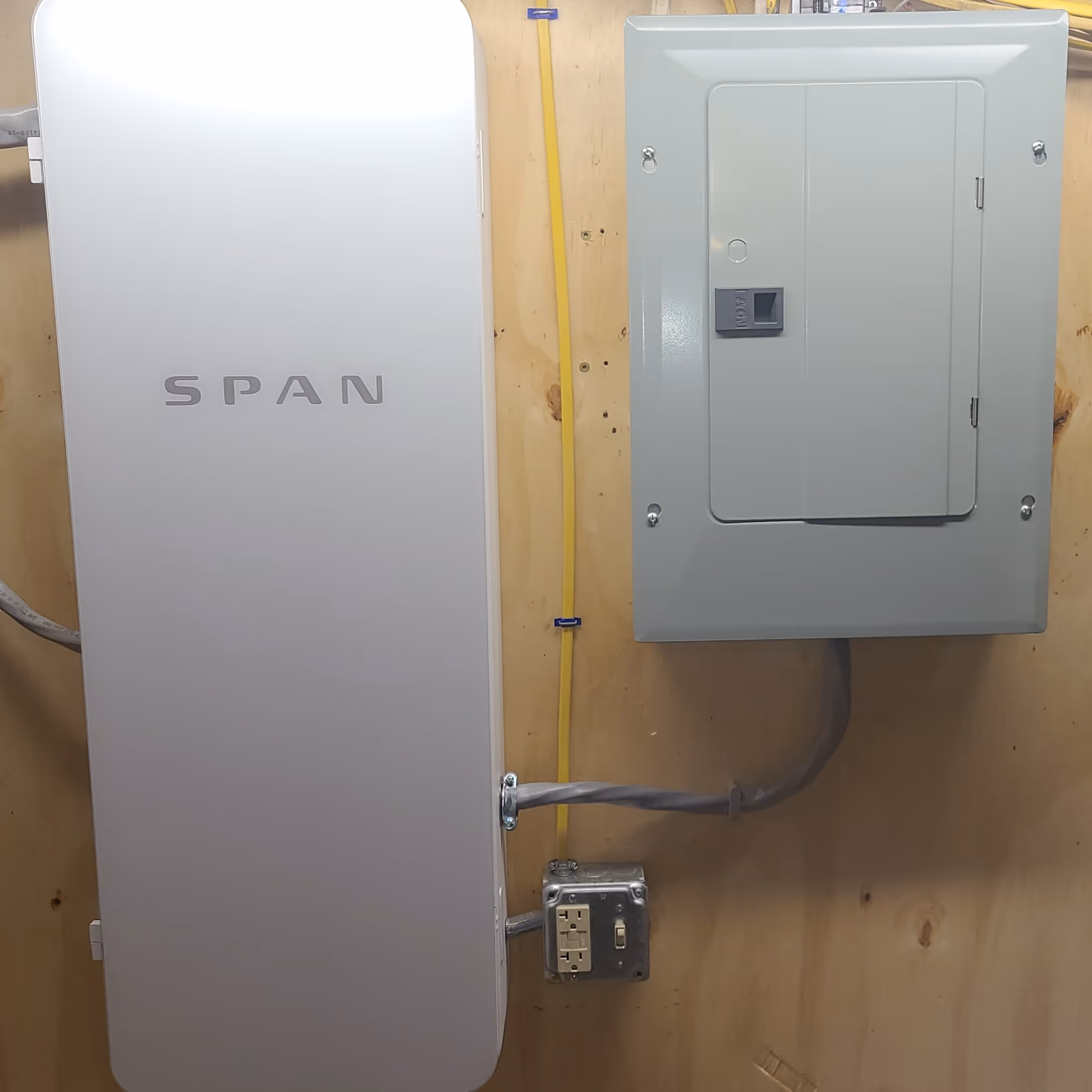 Span smart electrical panel installed on wood wall next to a traditional breaker box.