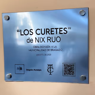 Placa metálica con la inscripción ‘LOS CURETES’ de Nix Ruo, obra donada a la Municipalidad de Bragado en agosto de 2021, con logotipos y un código QR.