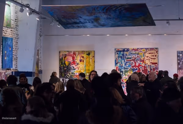 Personas de pie en un evento formal dentro de un edificio con paredes altas, columnas y obras de arte expuestas.