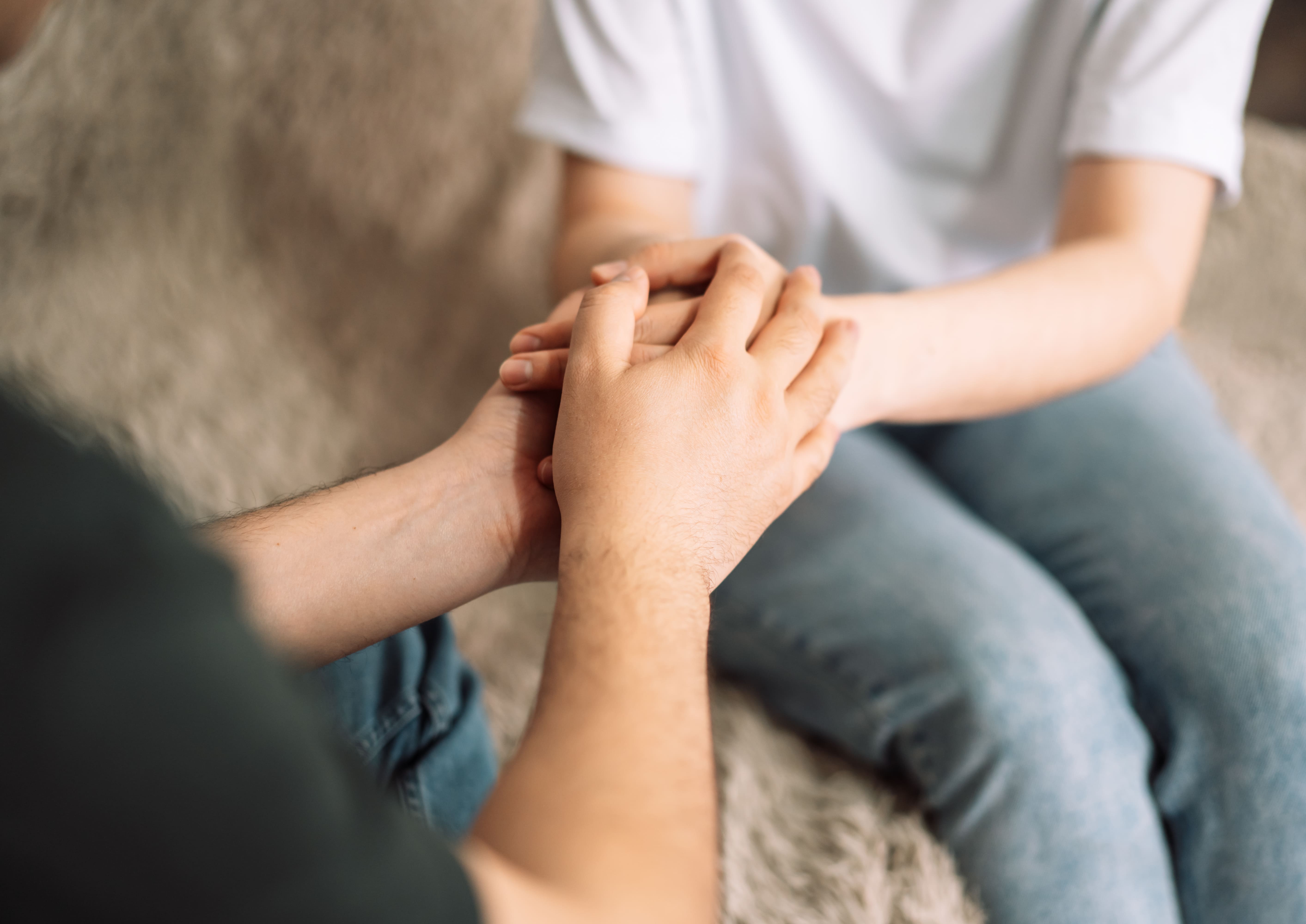A parent gently holds their teenager's hands while sitting together, offering comfort and reassurance.