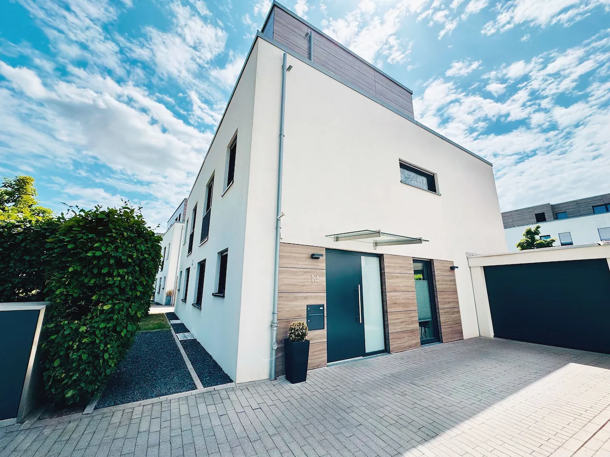 Modernes zweistöckiges Einfamilienhaus mit weißen Wänden, Holzverkleidung und Garage unter blauem Himmel.