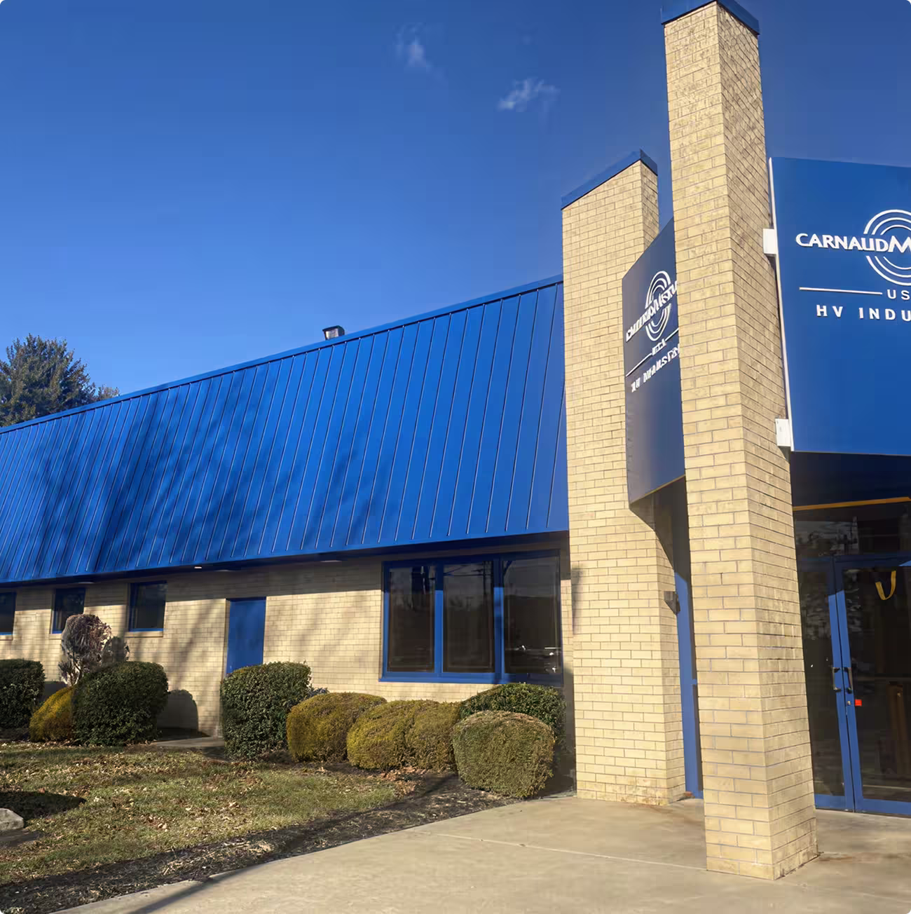 Brick building with blue metal roof and sign reading CarnaudMetalbox USA HV Industries.
