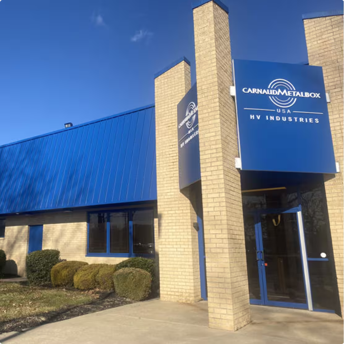Brick building with blue metal roof and sign reading CarnaudMetalbox USA HV Industries.