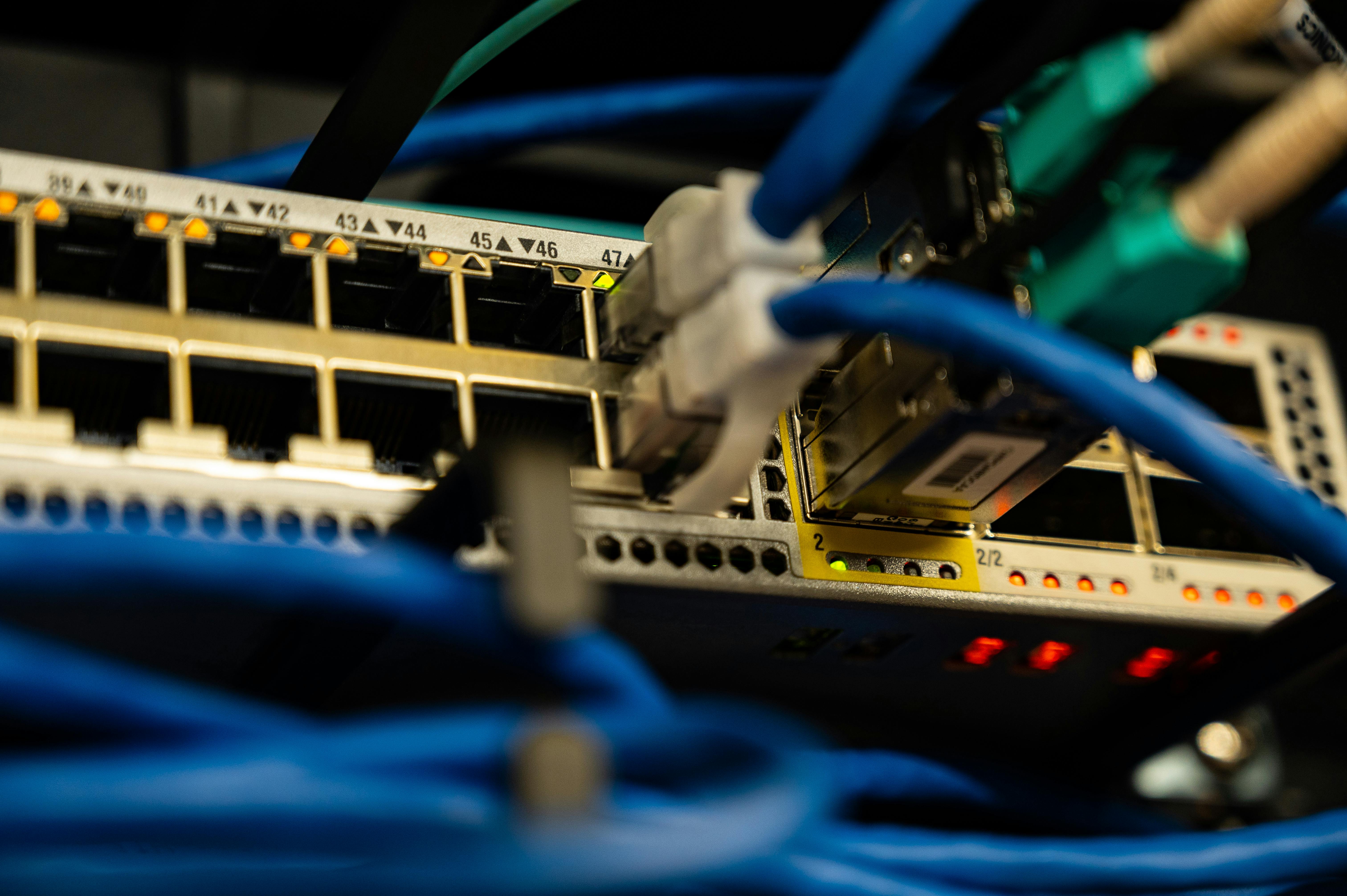 Close-up of network switch with multiple blue and green Ethernet cables plugged in and indicator lights.