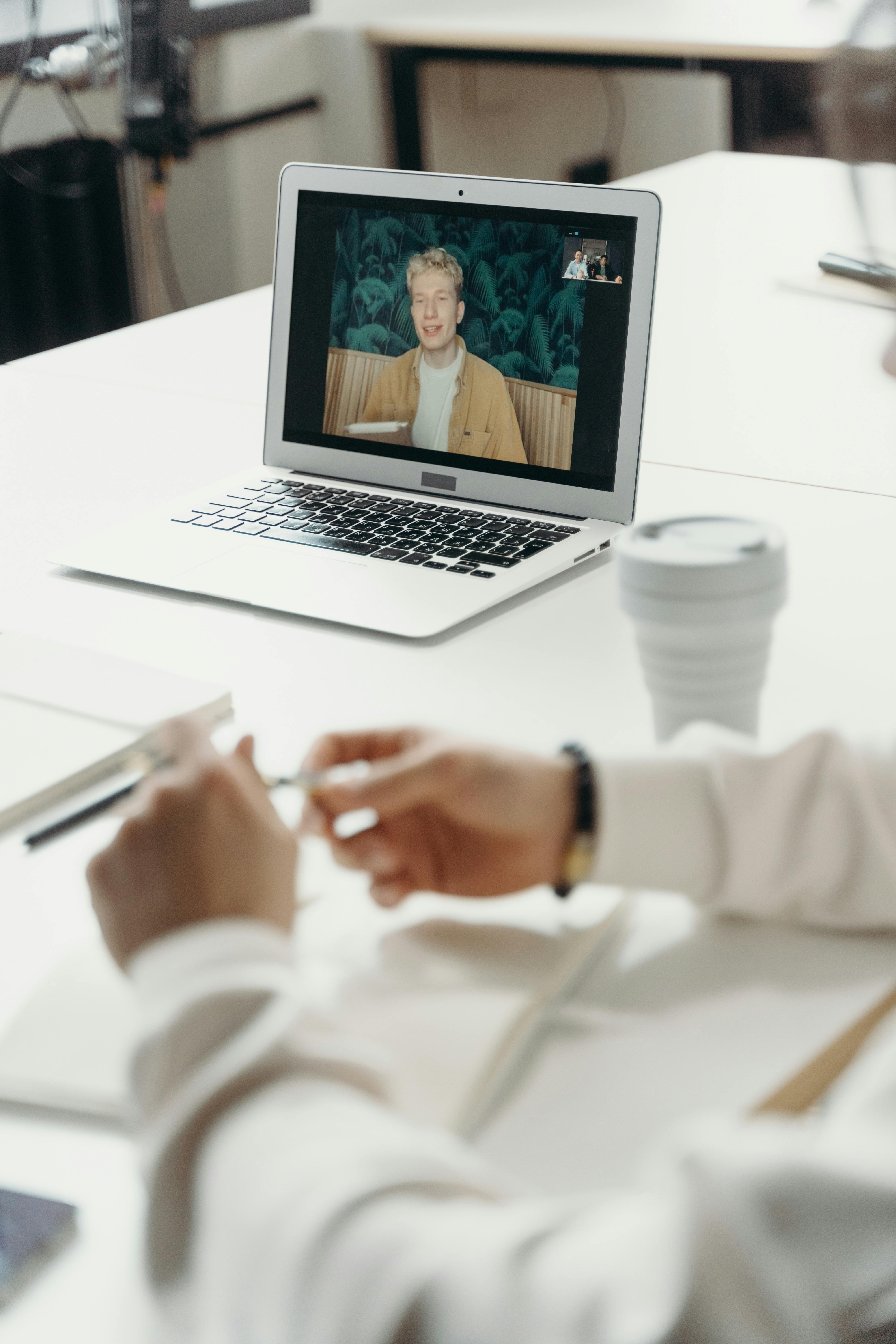 Person holding a pen during a video call on a laptop showing a young man speaking.