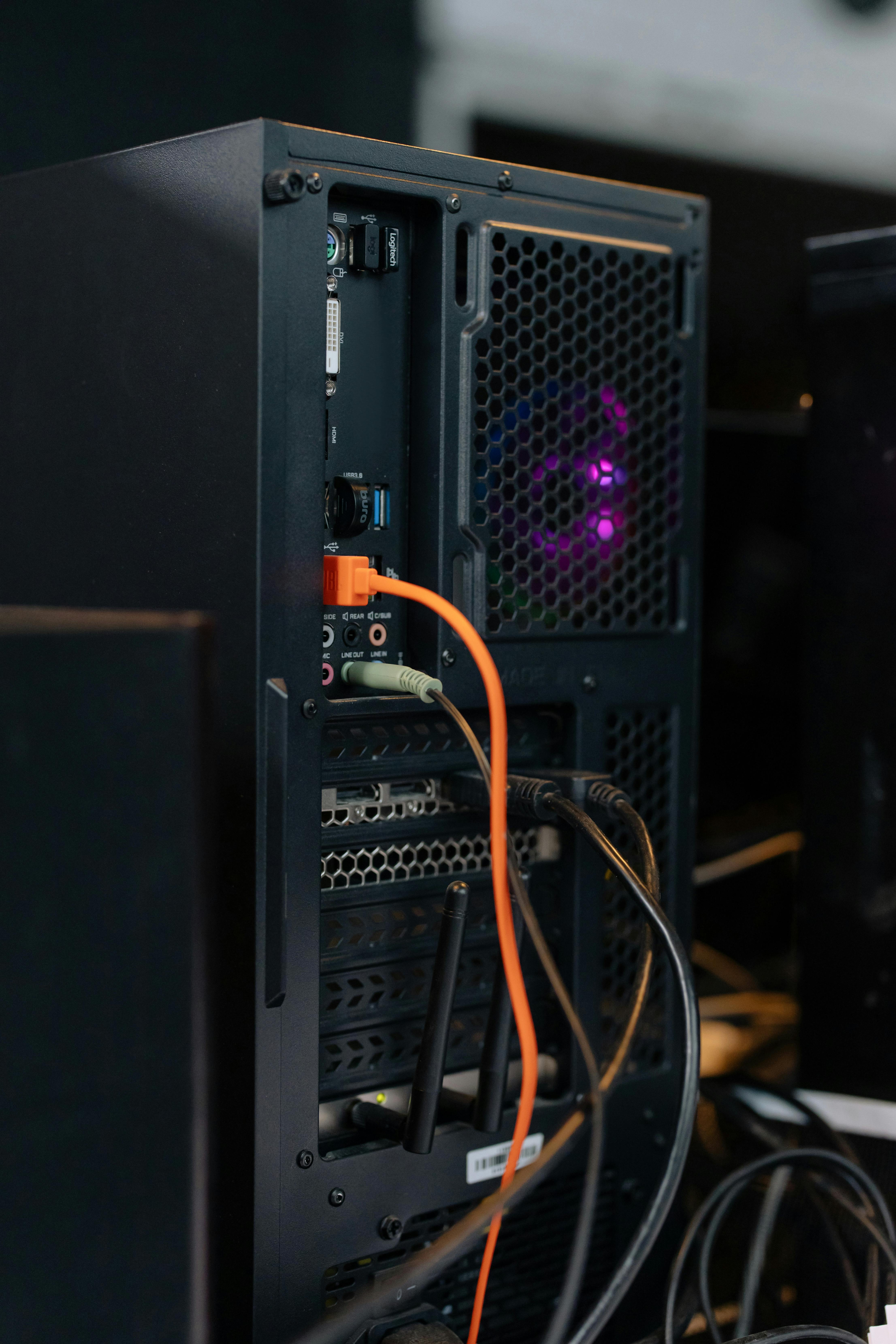 Back of a desktop PC case with multiple cables and antennas connected to various ports.