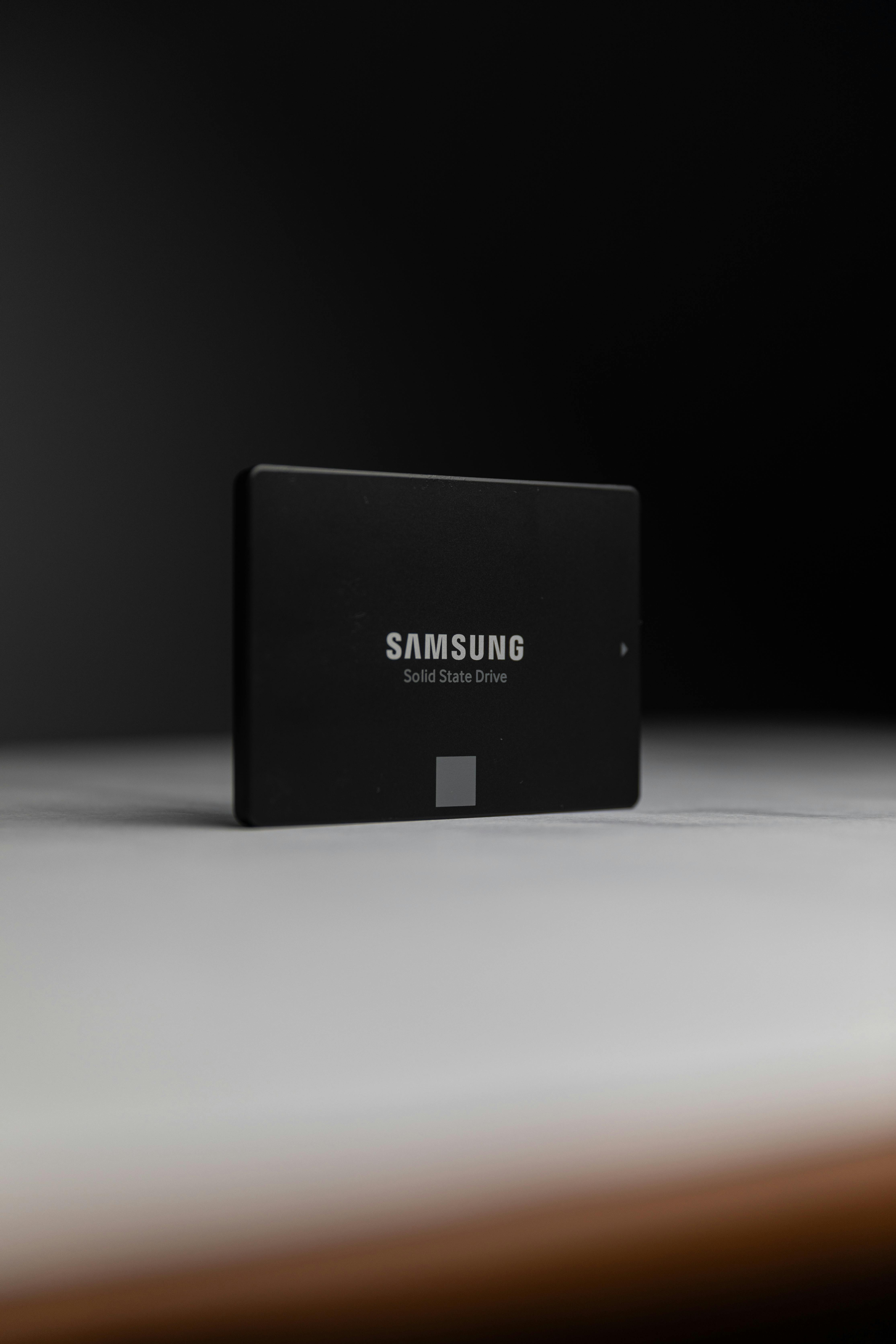Black Samsung solid-state drive standing upright on a light surface against a dark background.