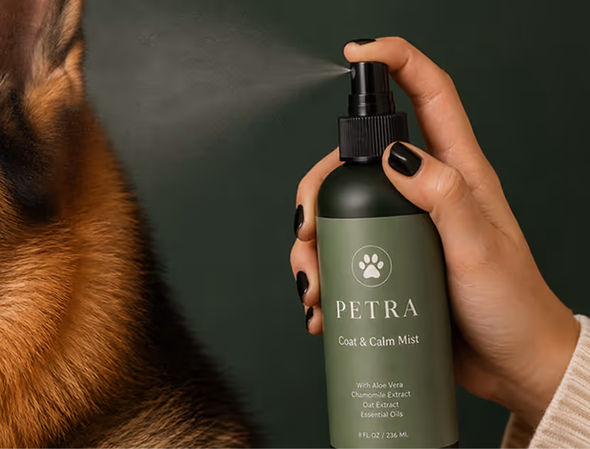 Hand spraying Petra Coat & Calm Mist on a dog's fur with a dark green backdrop.