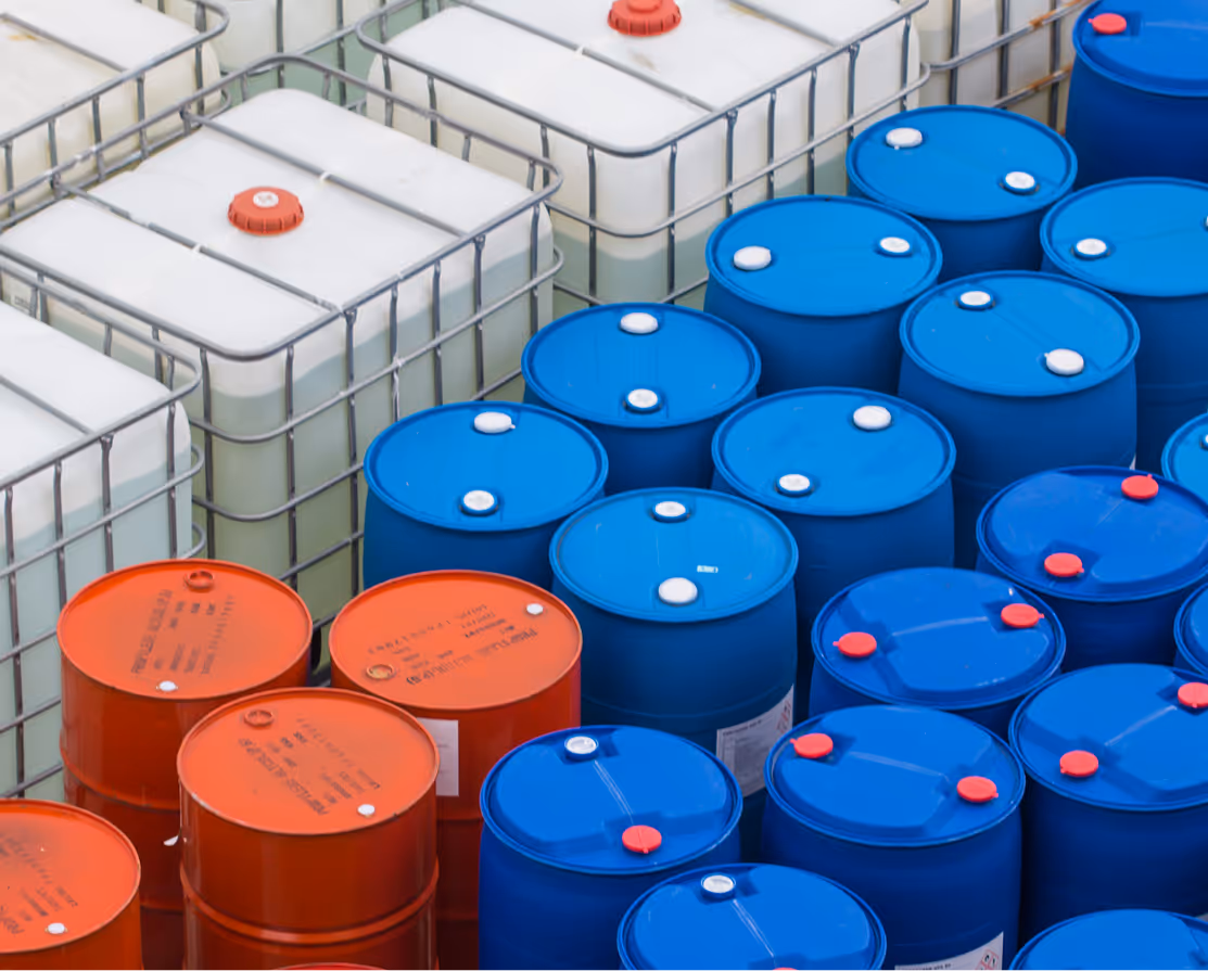 Grouped industrial containers including white liquid tanks, blue barrels, and red barrels with lids.