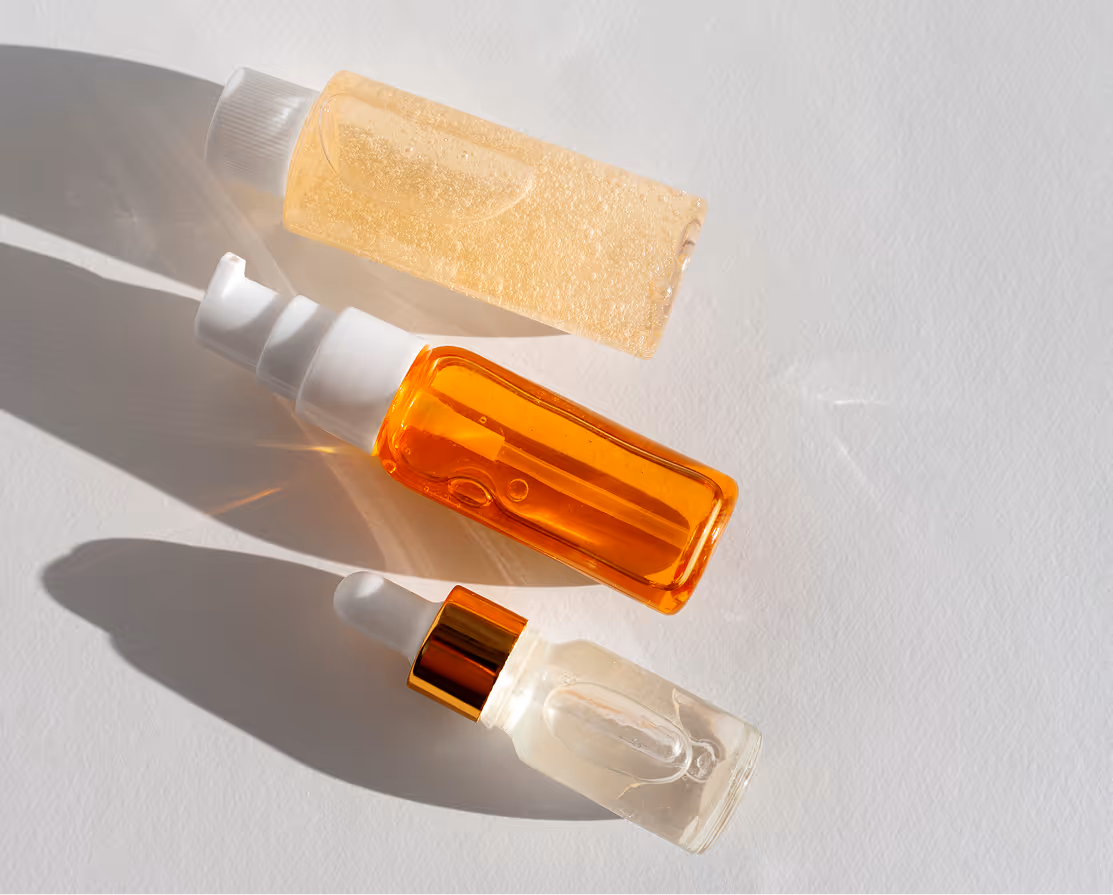 Three skincare bottles with clear, orange, and light yellow liquids on a white surface.