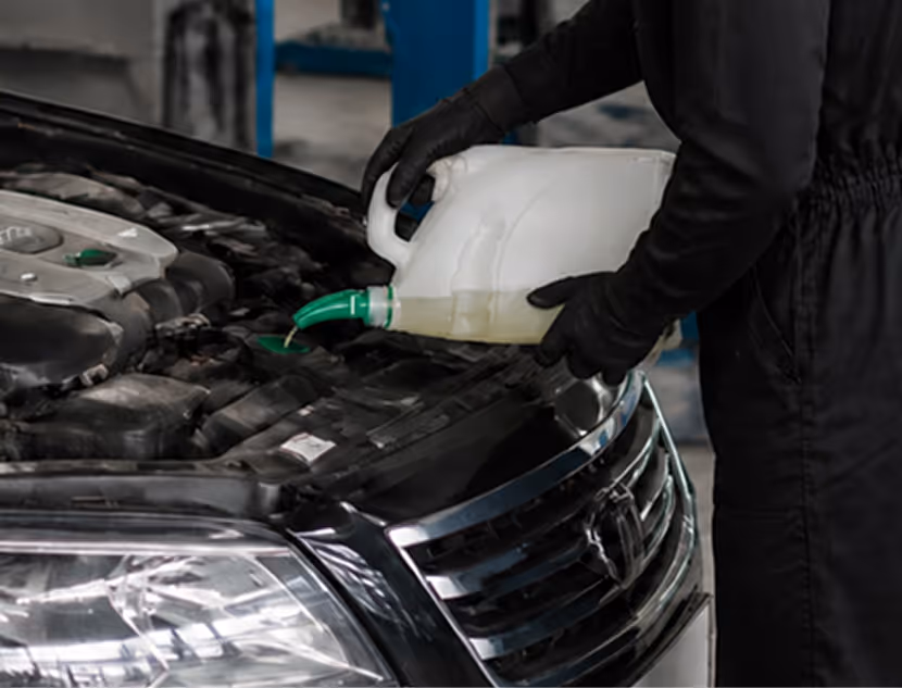 Person in black gloves pouring fluid from a white container into a car engine under the hood.