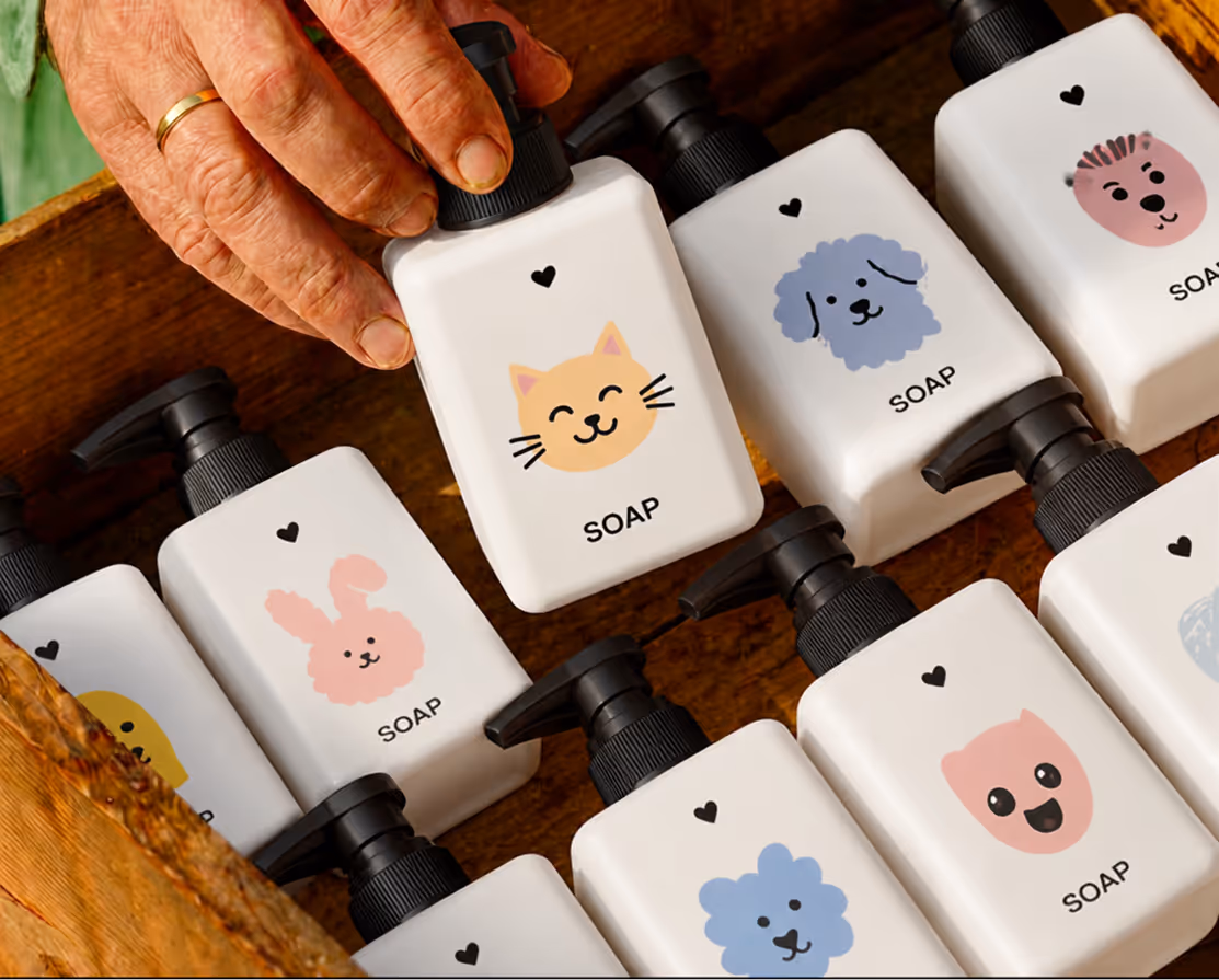 Hand picking a white soap bottle with cartoon cat face among various animal face soap bottles.