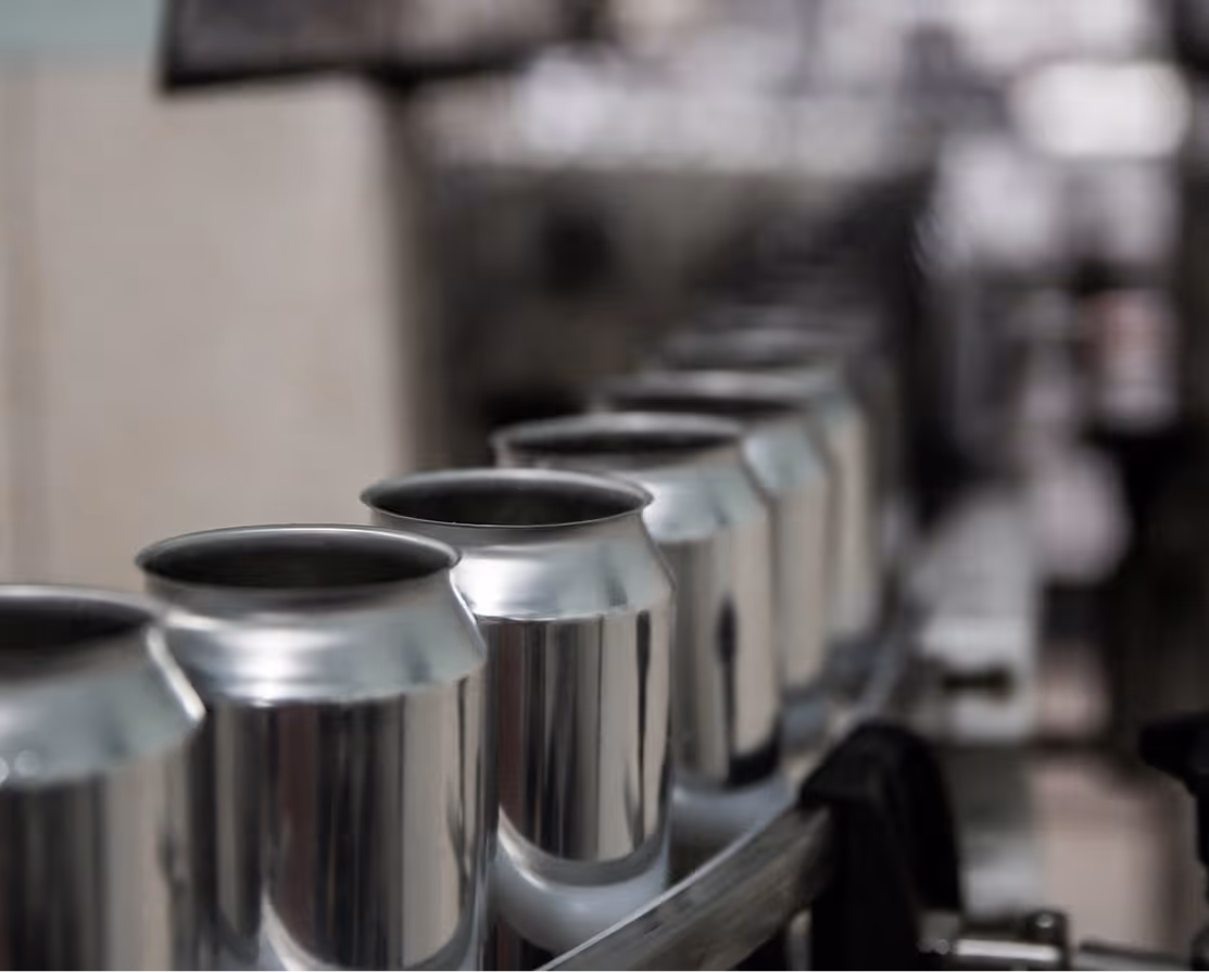 Row of empty aluminum cans on a conveyor belt in a beverage production line.