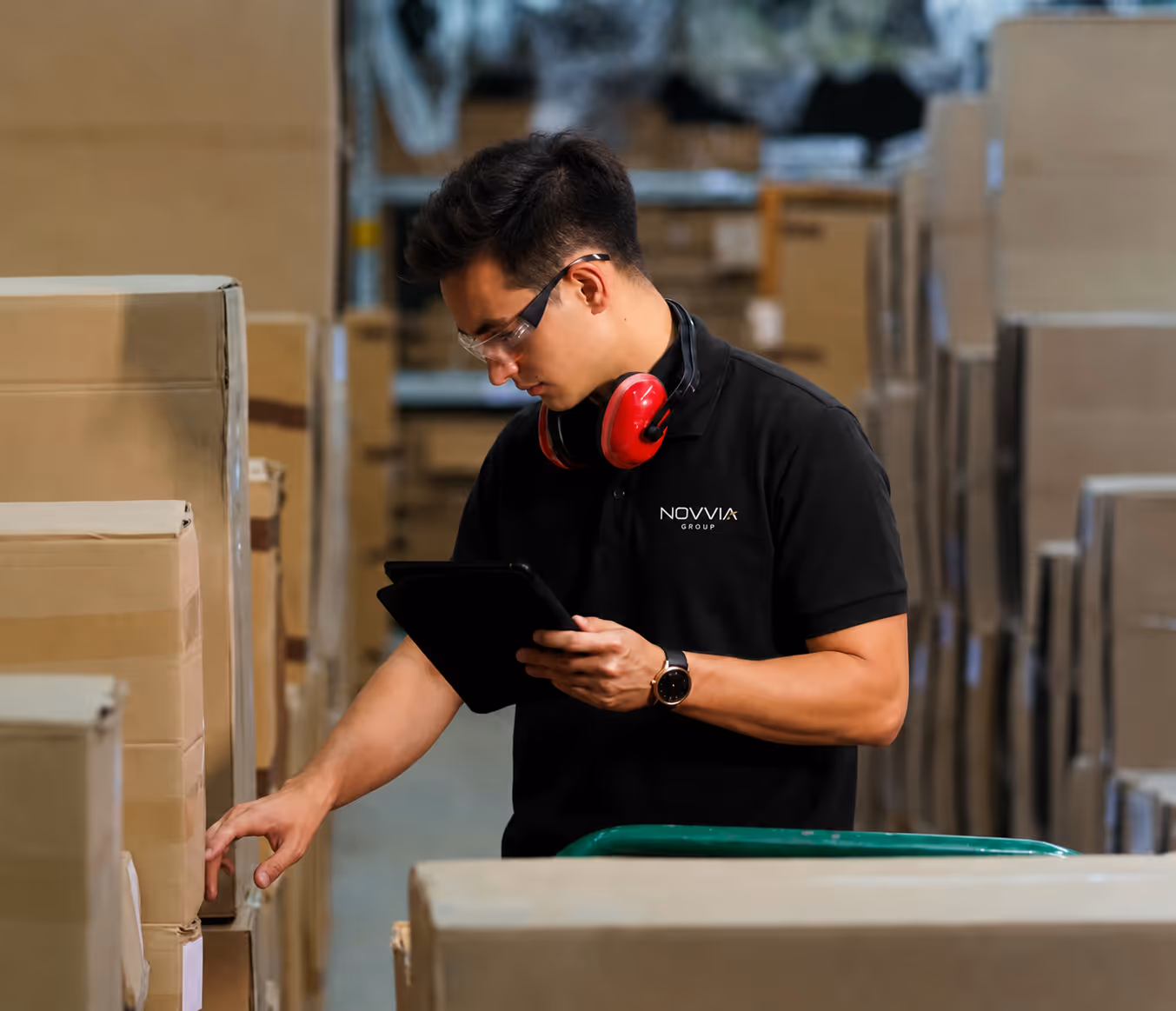 Warehouse worker in black shirt with headset checks boxes while holding a tablet.