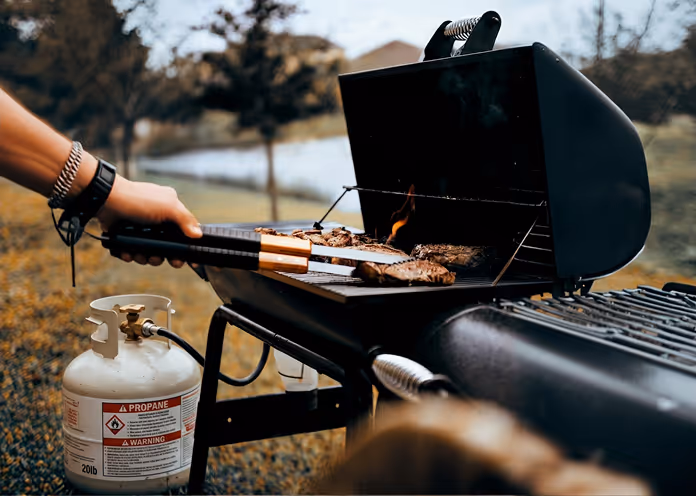 Person grilling meat on an open black propane gas grill outdoors.