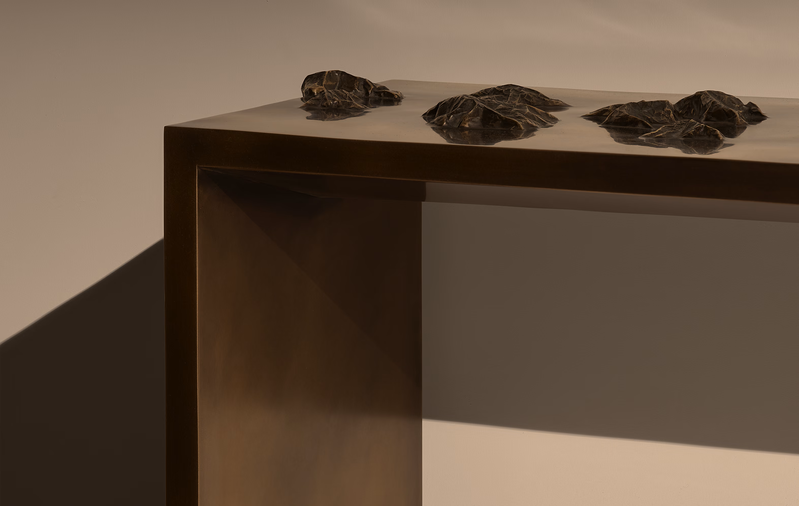 Minimalist dark brown console table with a smooth surface featuring three small, irregularly shaped black rock-like sculptures on top, set against a neutral beige background with soft shadows.