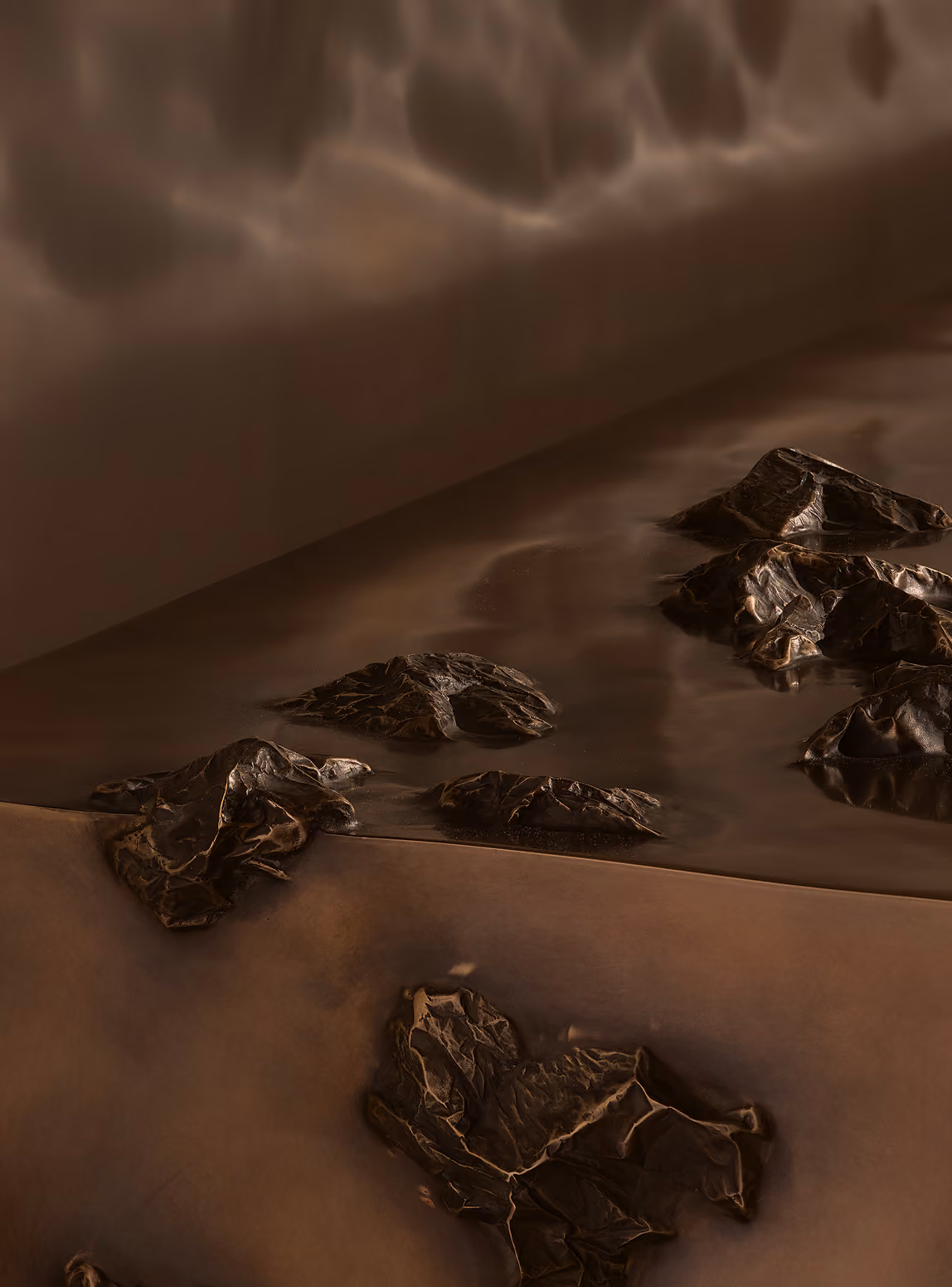 Close-up of a bronze or metallic relief sculpture featuring textured mountainous or rocky terrain with various elevations casting shadows.