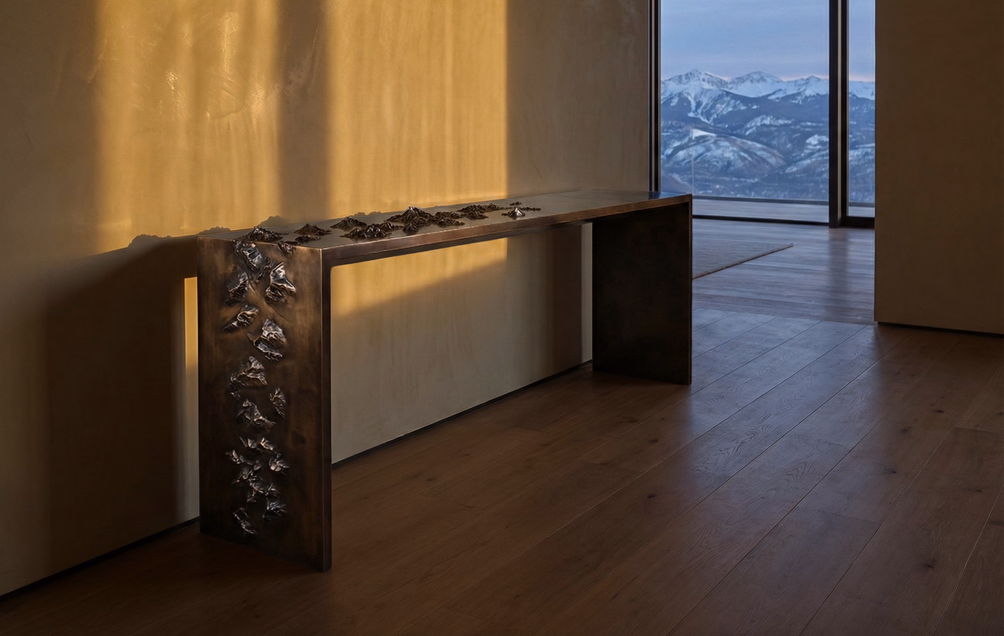 Modern minimalistic wooden bench with metallic decorative details along the left leg and top edge, placed indoors on a wooden floor with a beige wall behind it, and a large window showing snowy mountain peaks in the distance.
