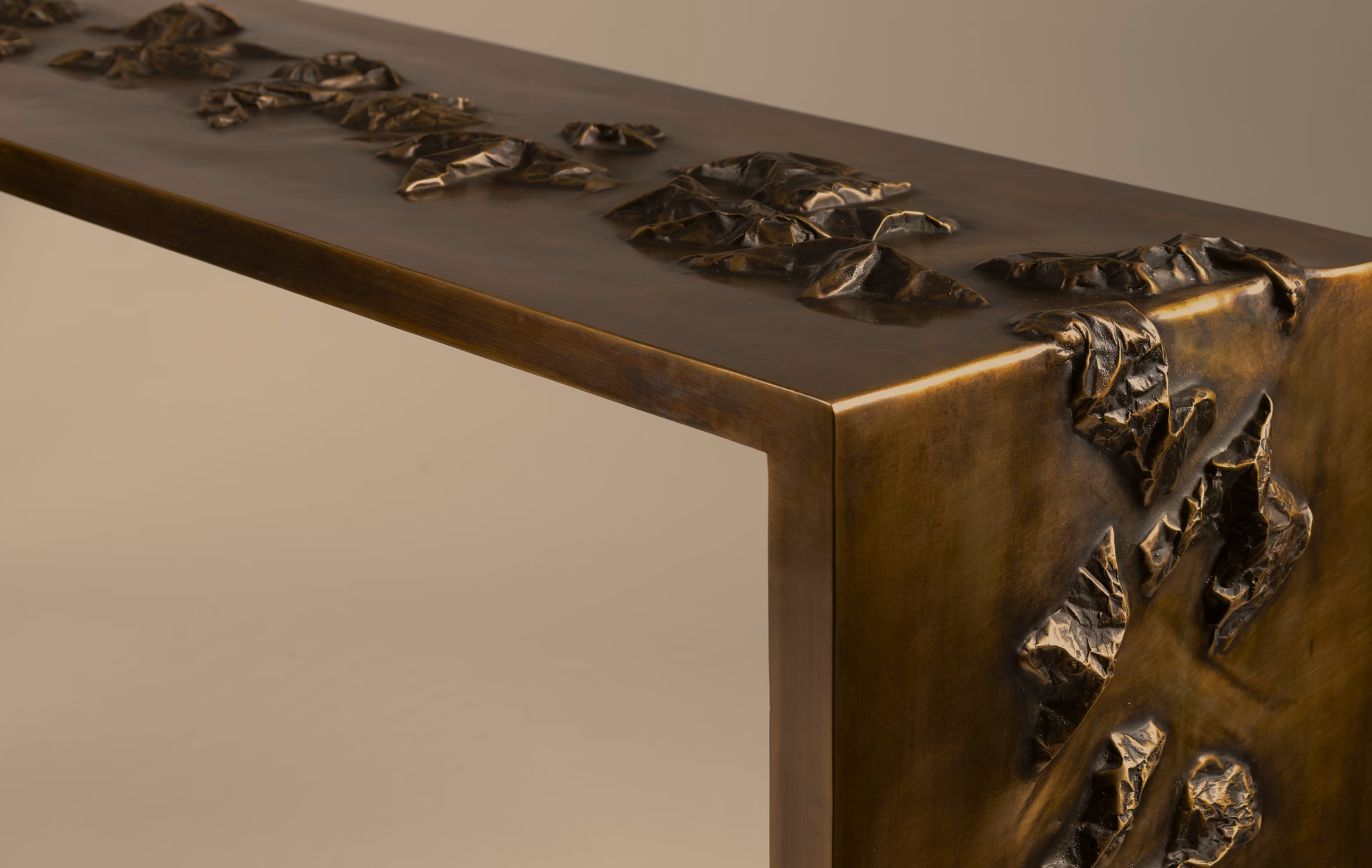 Close-up of a bronze-colored metal table with textured, crumpled leaf-like designs embedded on its top and side edges.