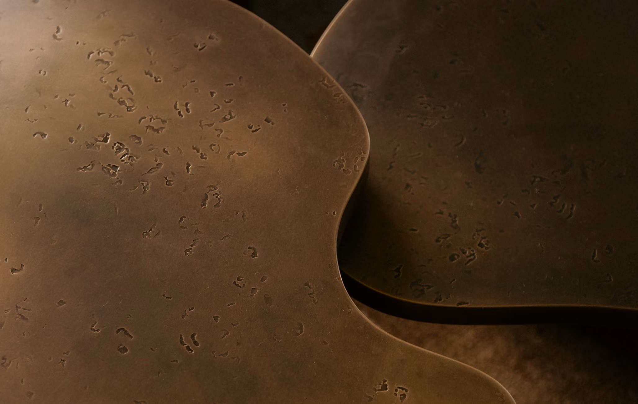 Close-up of two overlapping metallic surfaces with a bronze color and a textured, worn pattern.