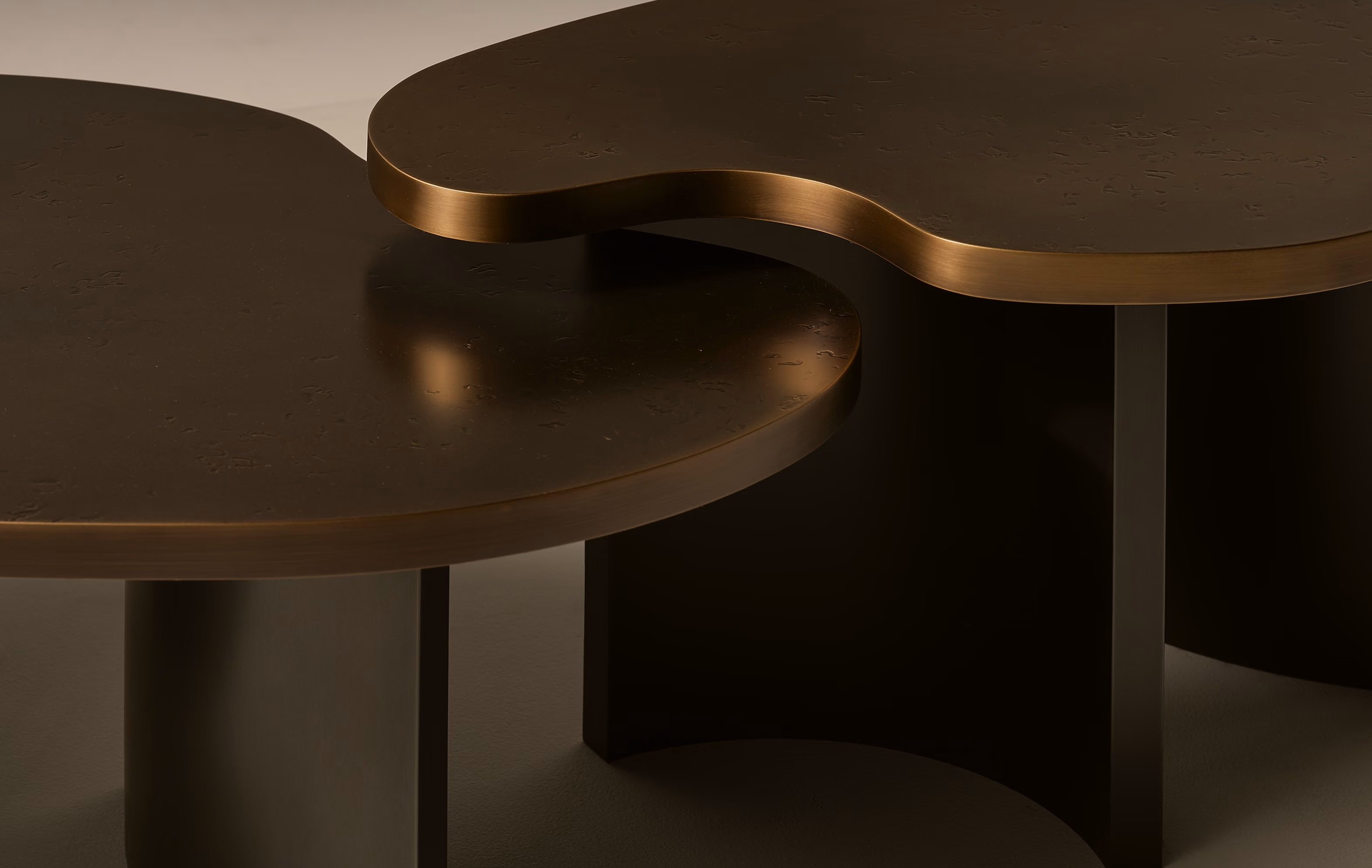 Close-up of two dark brown wooden tables with rounded, organic edges and cylindrical supports, showcasing smooth surfaces and a minimalist design.
