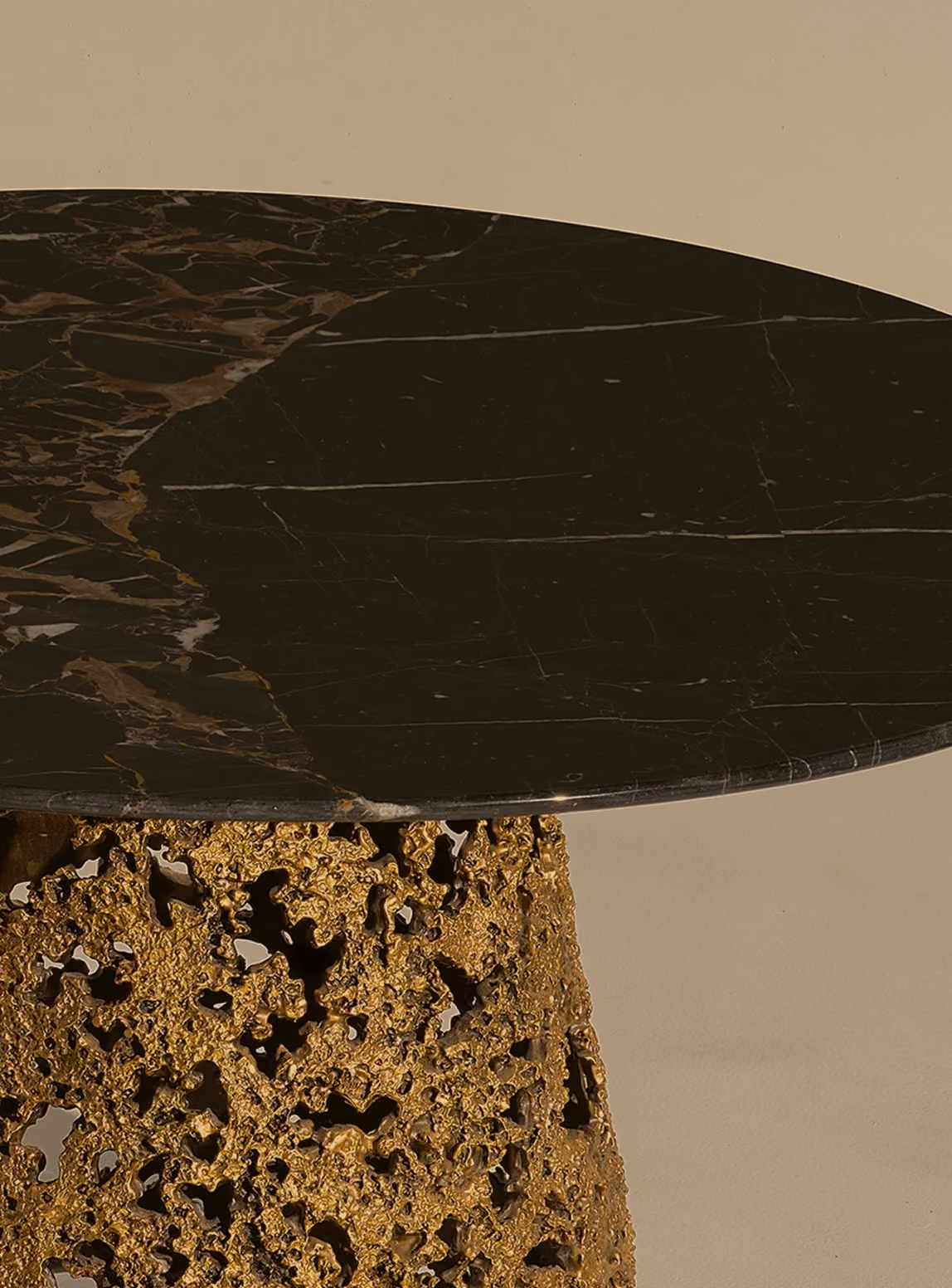 Close-up of a table with an oval black marble top and a textured gold metallic base featuring intricate irregular patterns and holes.