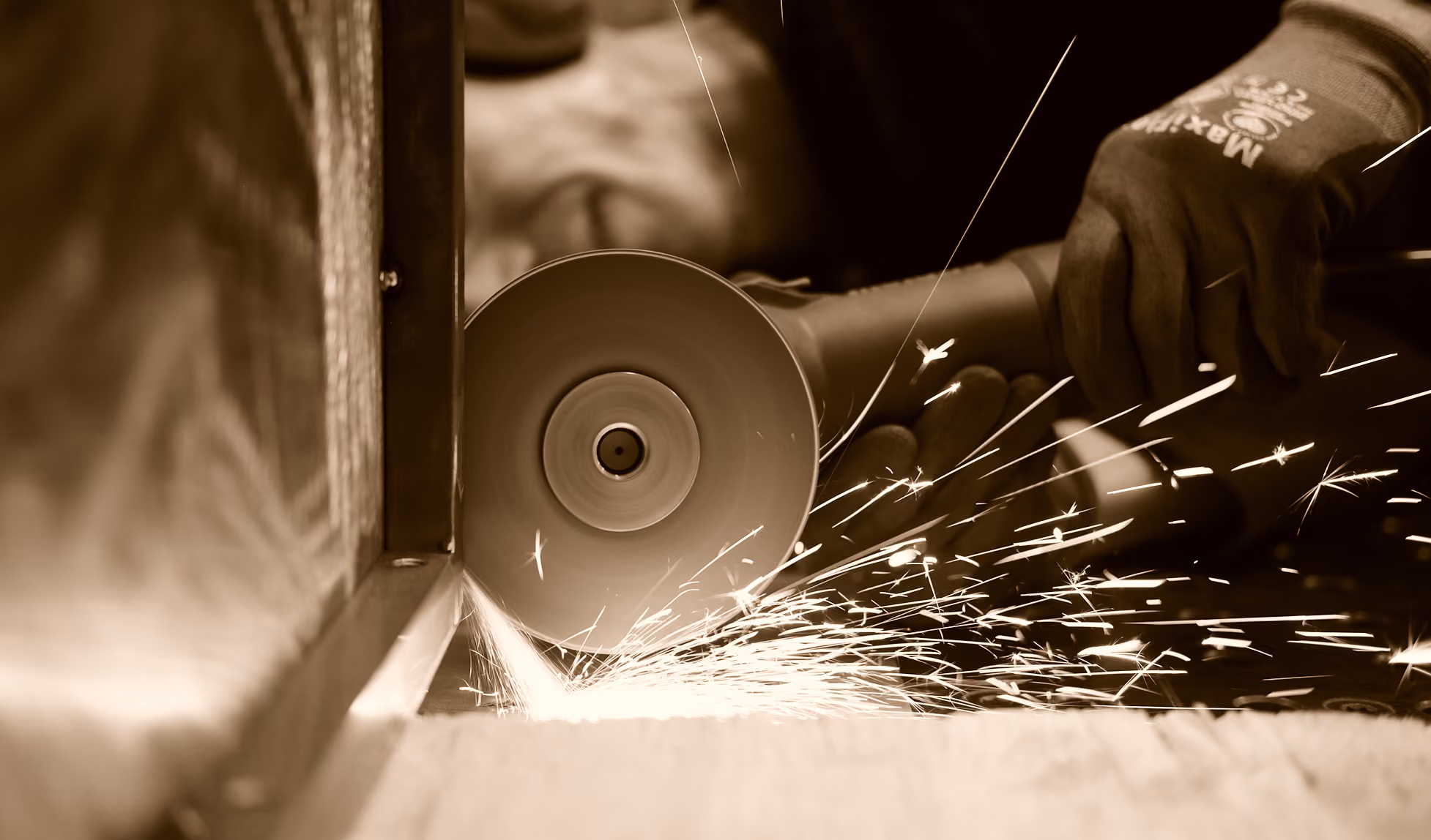 Close-up of a person using an angle grinder on a metal surface, creating bright sparks flying outward.