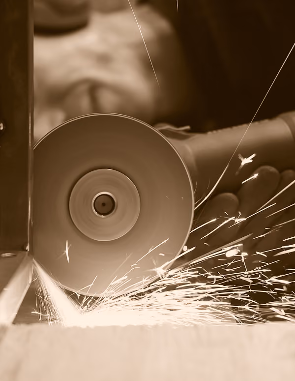 Close-up of a worker using a handheld angle grinder producing bright sparks while cutting or grinding metal.