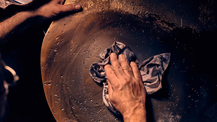 A pair of hands cleaning a large, round clay pot with a cloth in dim light.