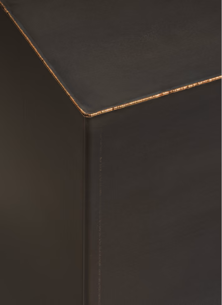 Close-up view of the corner of a black cube-shaped stool with a slightly worn edge showing a brownish layer underneath the black surface.
