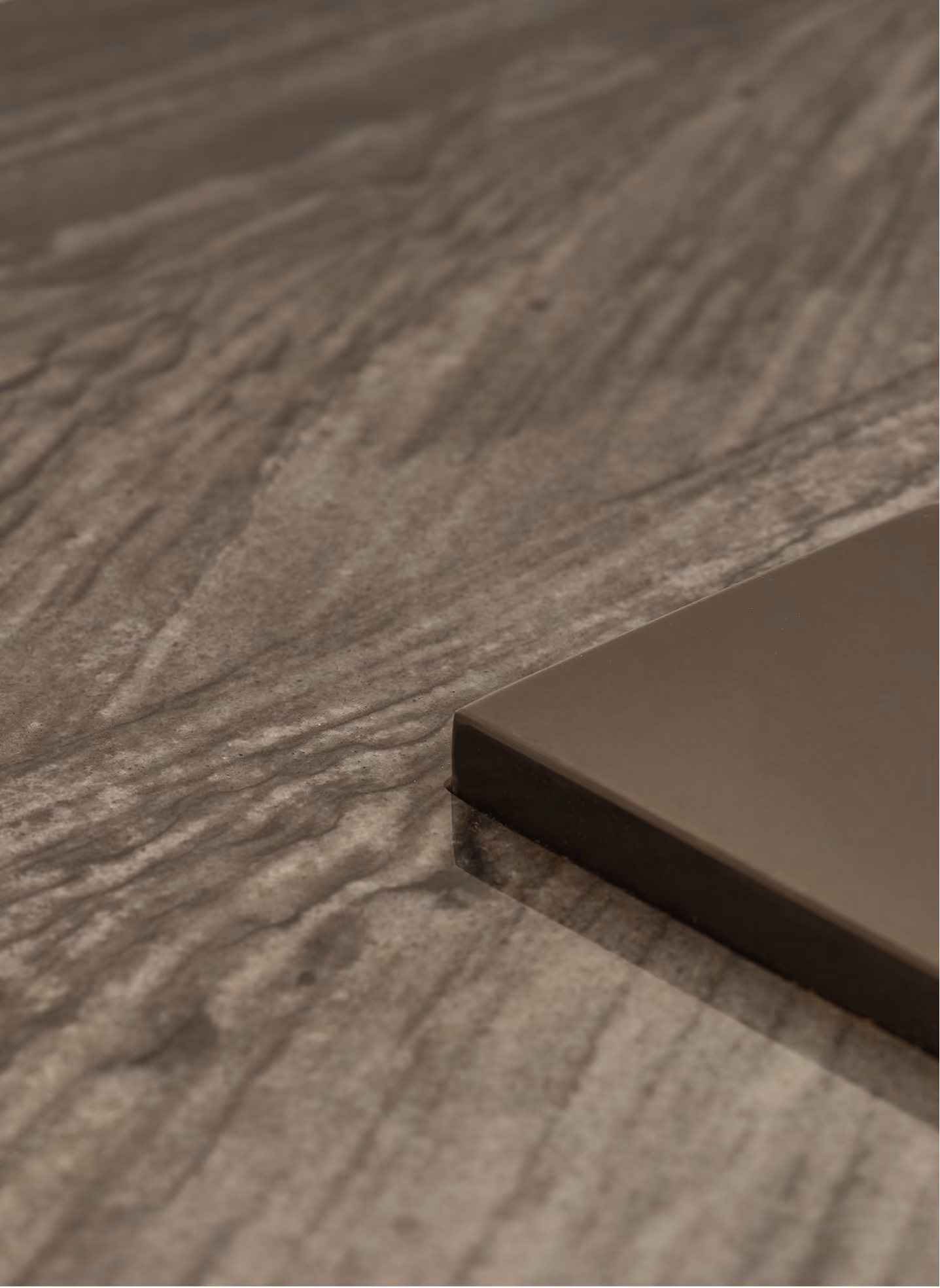 Close-up of a smooth, polished dark wood surface next to a flat, rectangular metal edge in matte finish.