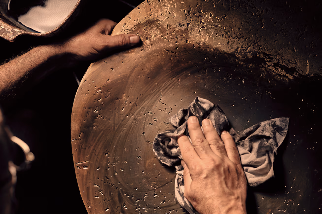 Two hands working on a large pottery wheel, shaping and smoothing clay with a cloth in warm lighting.