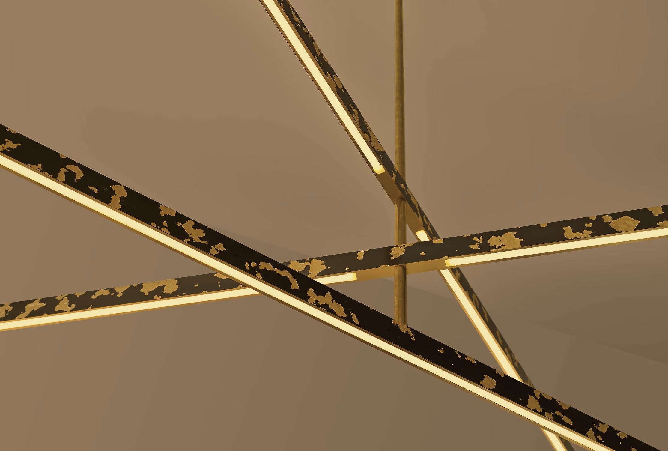 Modern chandelier with intersecting elongated rectangular light bars in black with gold peeling effect, hanging from the ceiling against a beige background.
