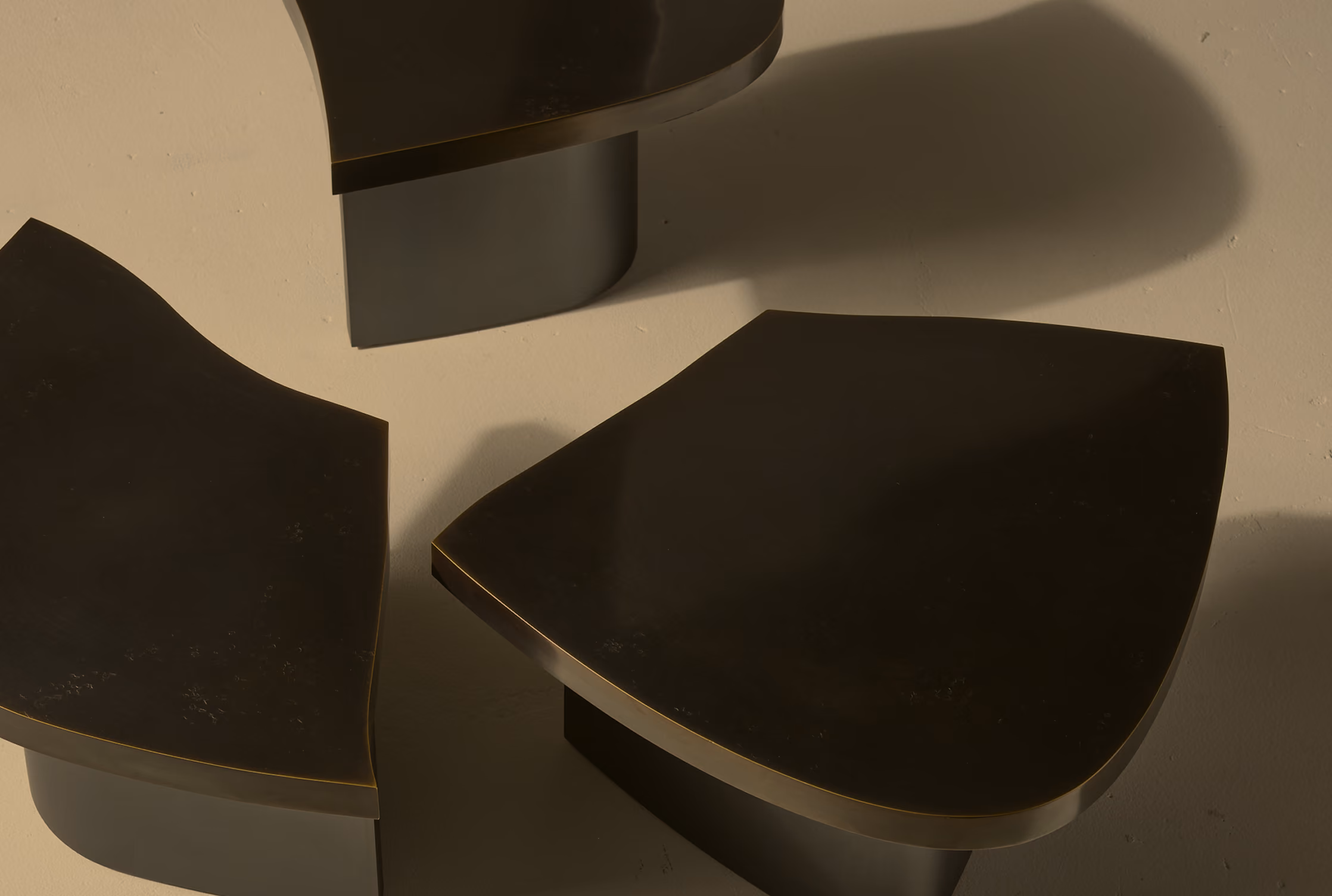 Close-up of three glossy black sculptural objects with curved edges placed on a beige surface casting soft shadows.