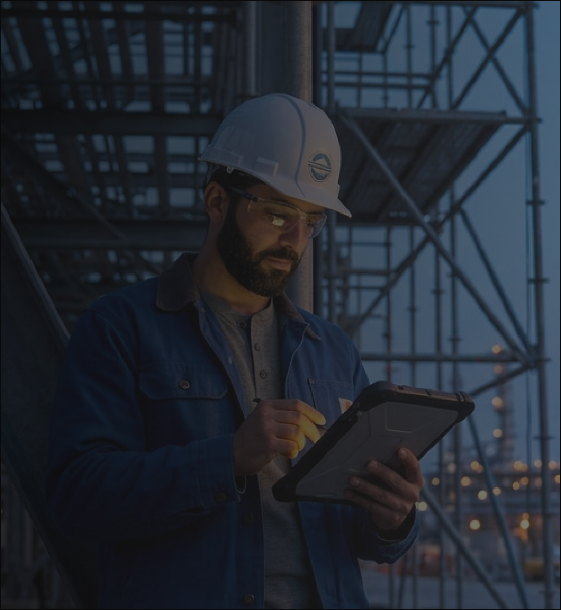 Construction estimator in a hard hat and safety glasses reviewing an estimate on a rugged tablet at a job site at dusk