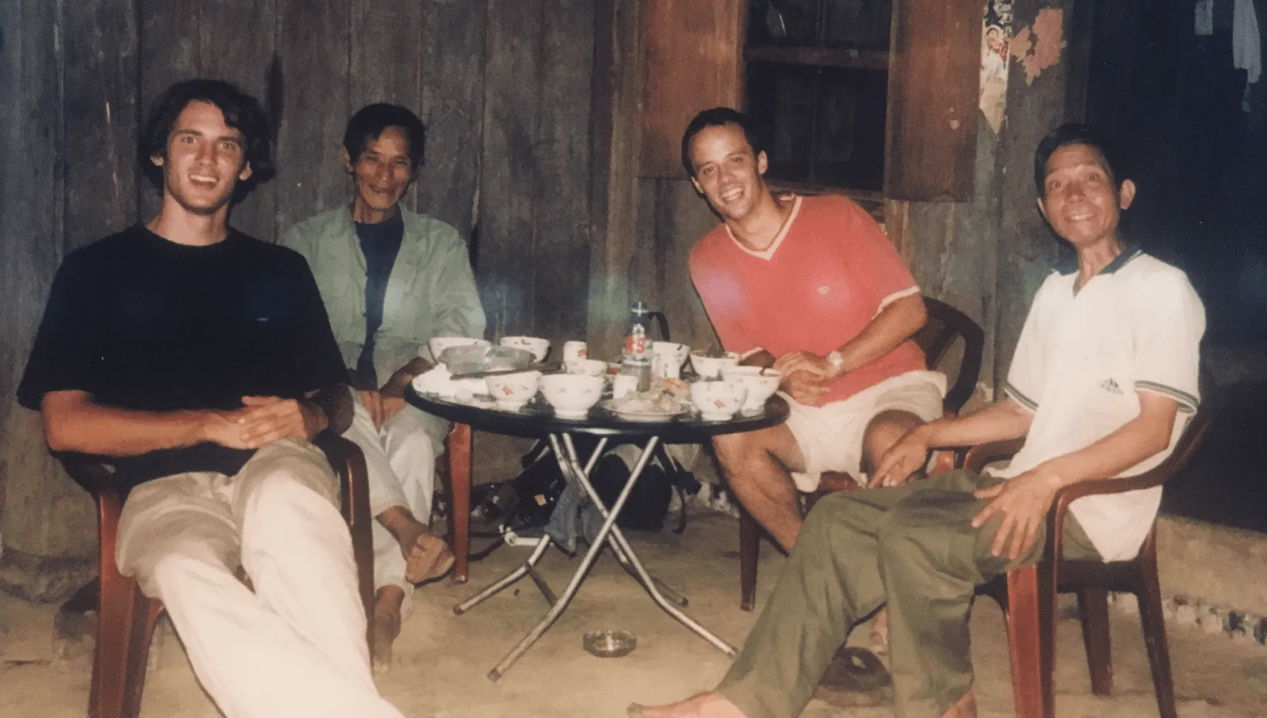 Quatre hommes assis autour d'une table ronde avec des bols et des tasses à l'extérieur.