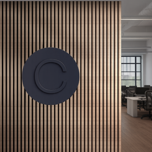 Dark circular sign with letter C on vertical wooden slat wall in modern office space.