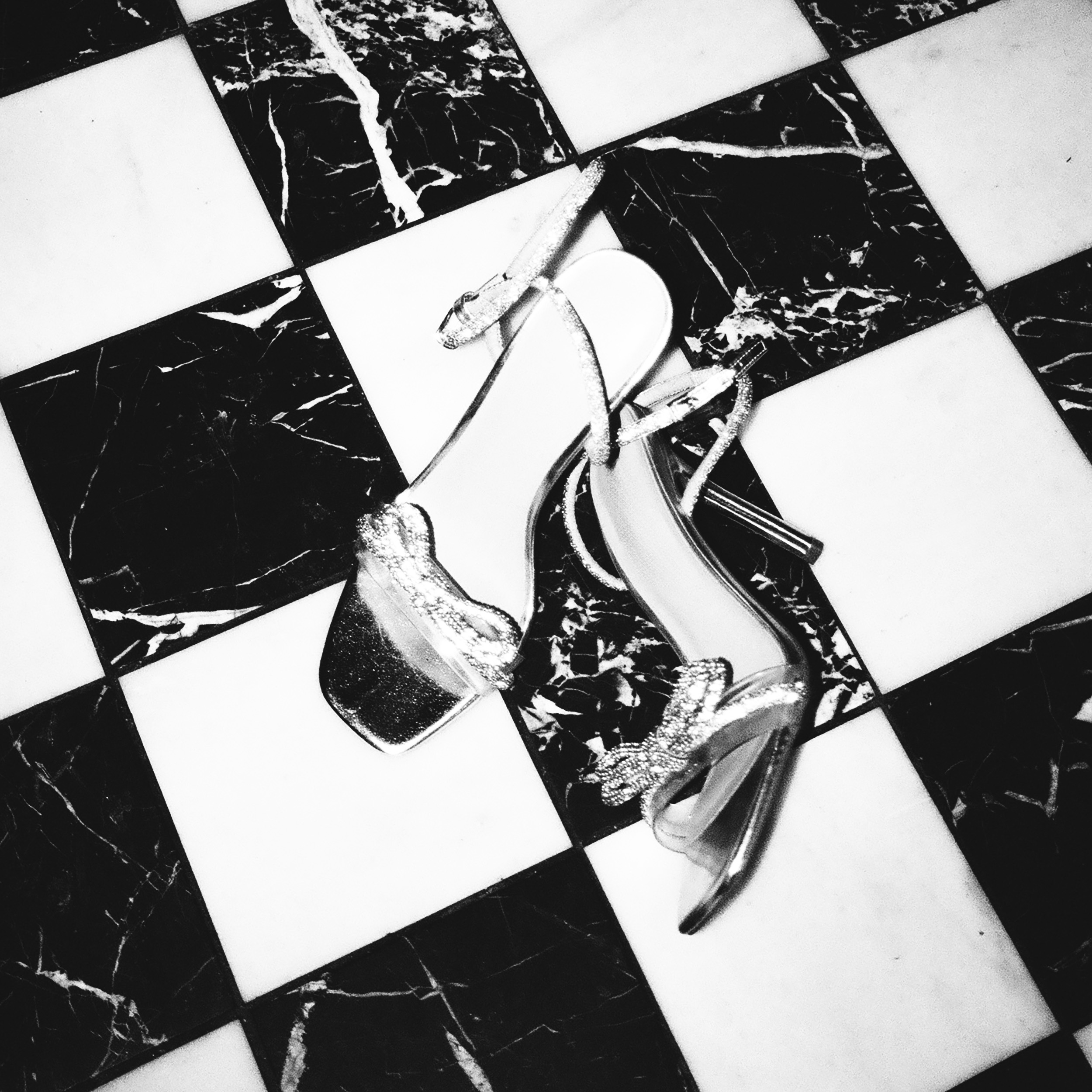 Pair of sparkly high-heeled sandals on a black and white checkered marble floor.
