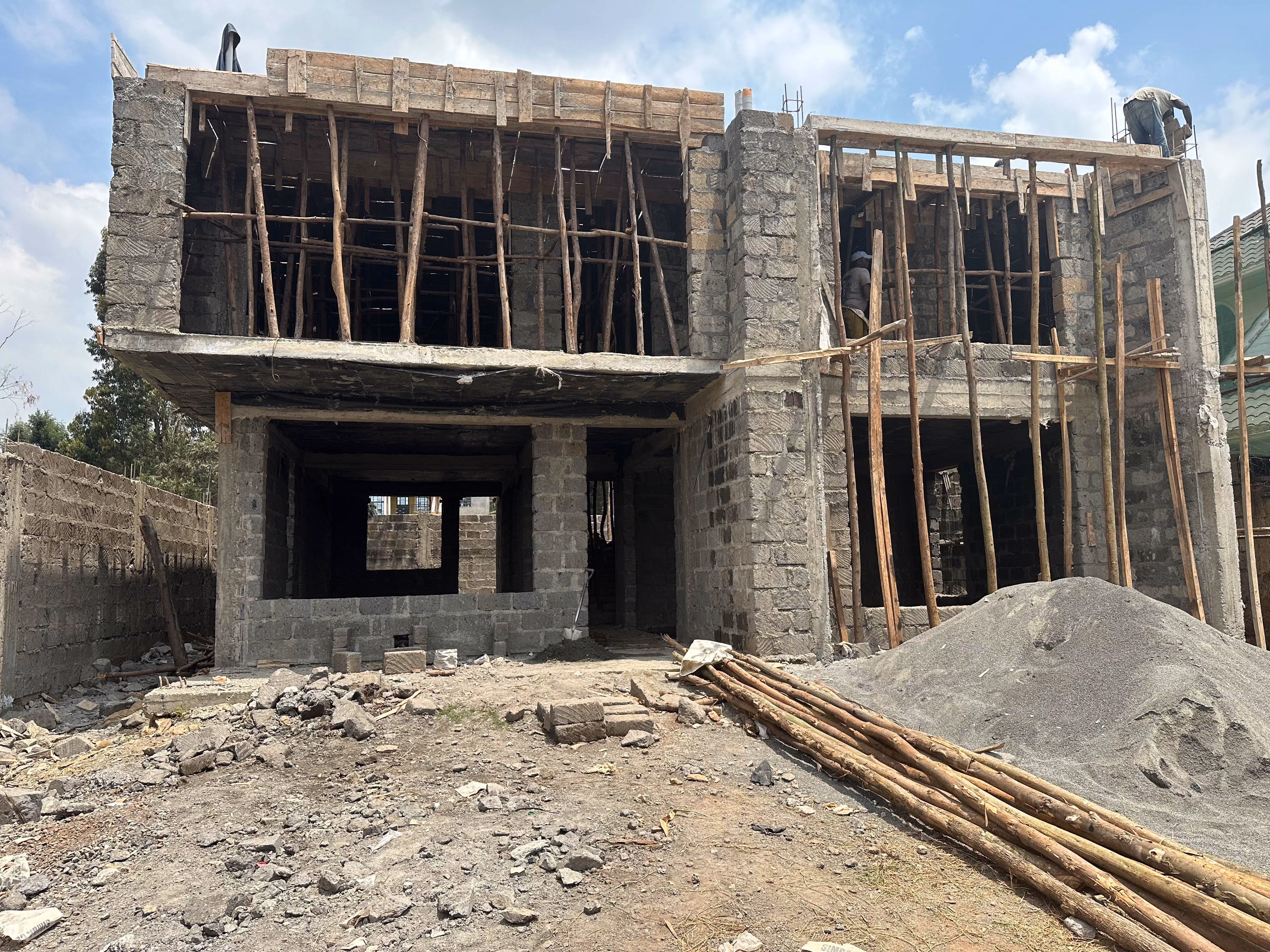 Two-story concrete structure under construction with wooden scaffolding and workers on site.