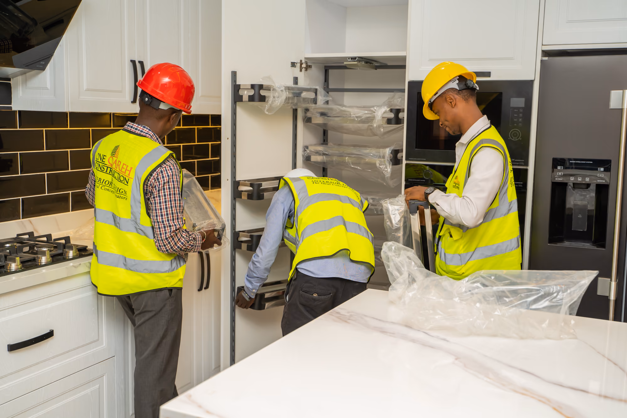 Three construction workers installing kitchen cabinet shelving inside a modern kitchen.