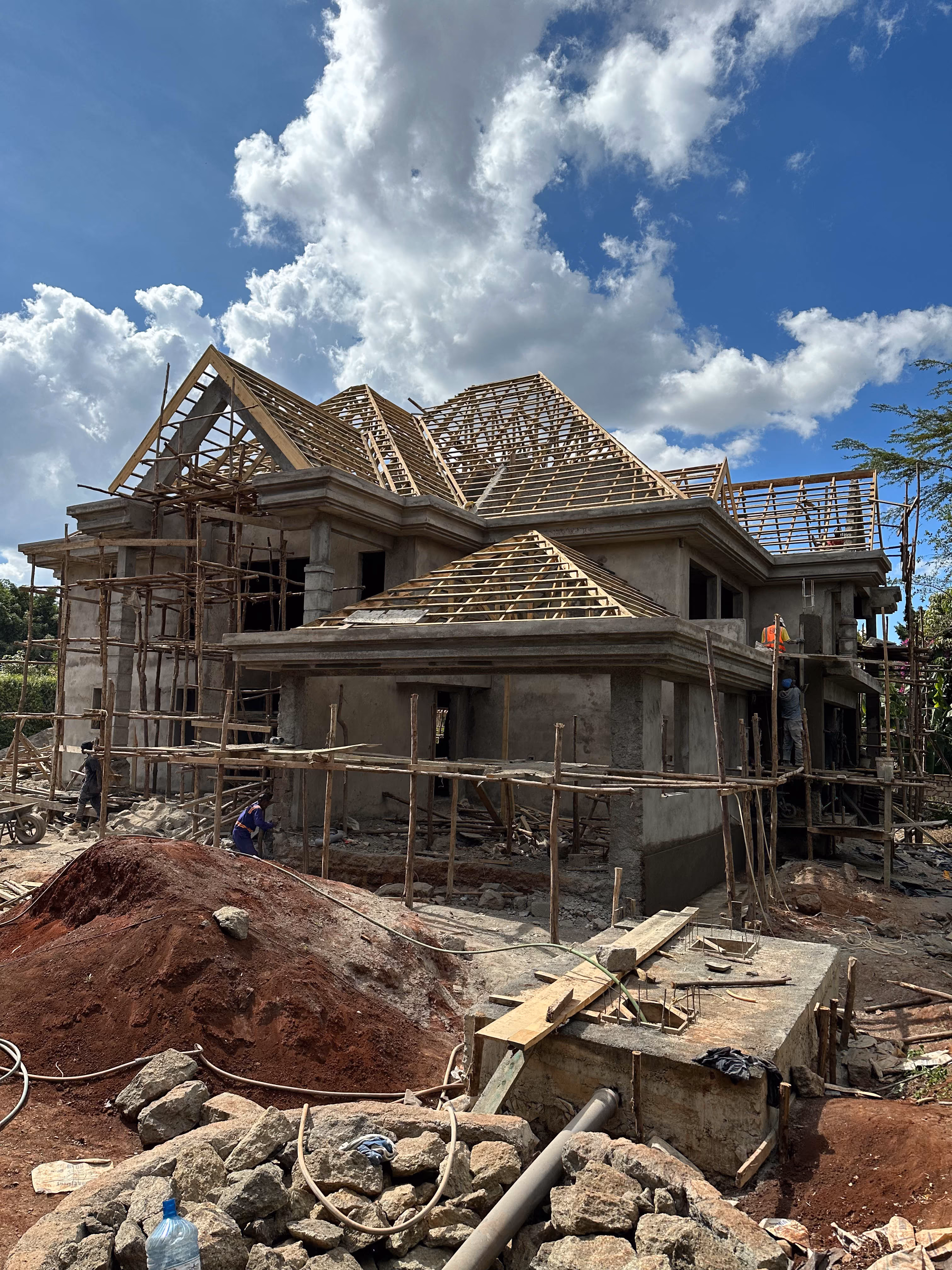 Two-story house under construction with wooden roof framing and scaffolding under a partly cloudy sky.