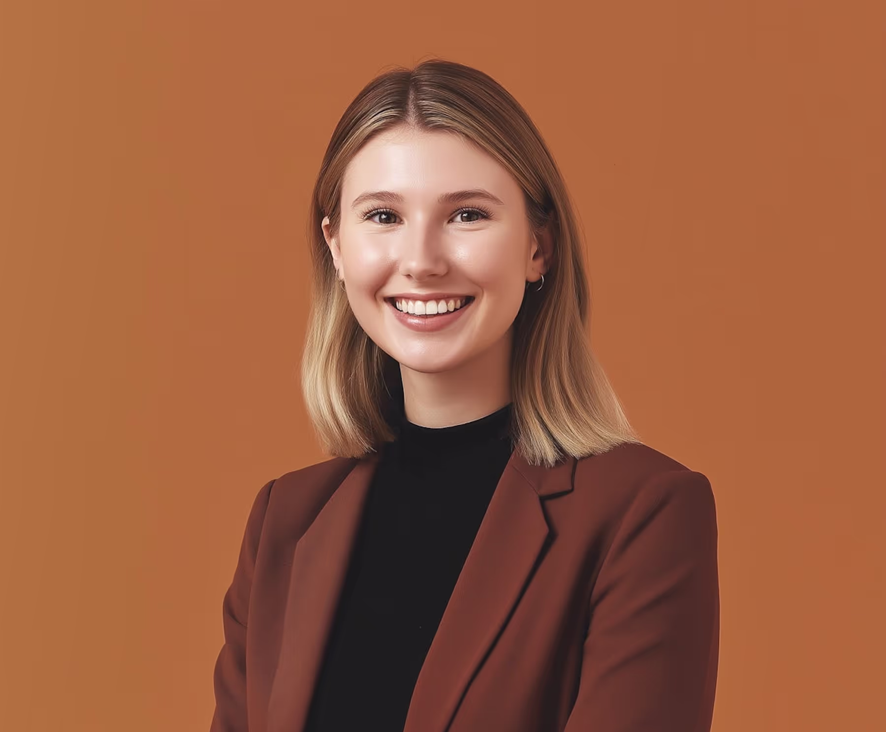 Smiling young woman with shoulder-length blonde hair wearing a black top and brown blazer against a brown background.