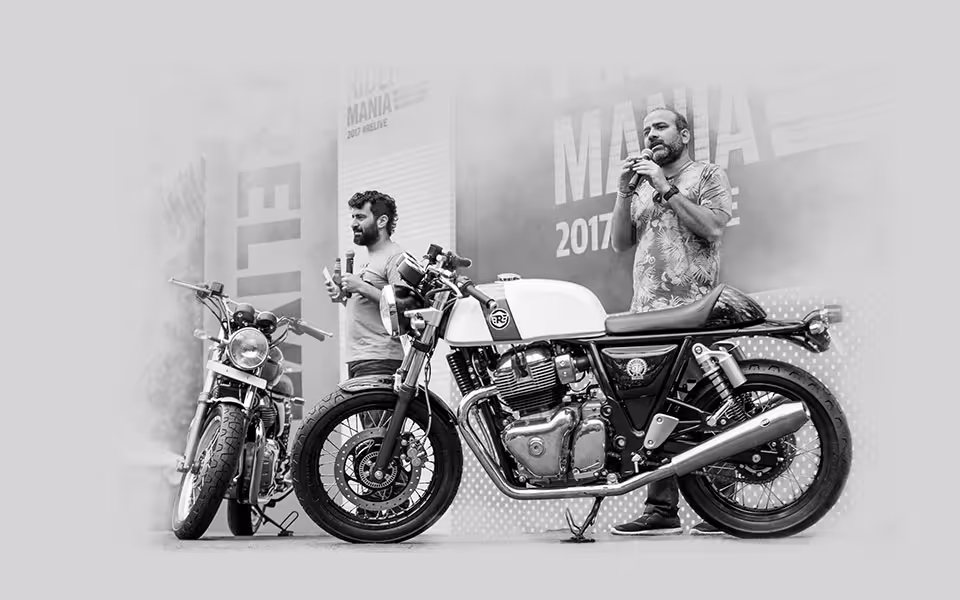 Dvaja muži prezentujú dve motocykle Royal Enfield na podujatí s mikrofónmi v rukách.