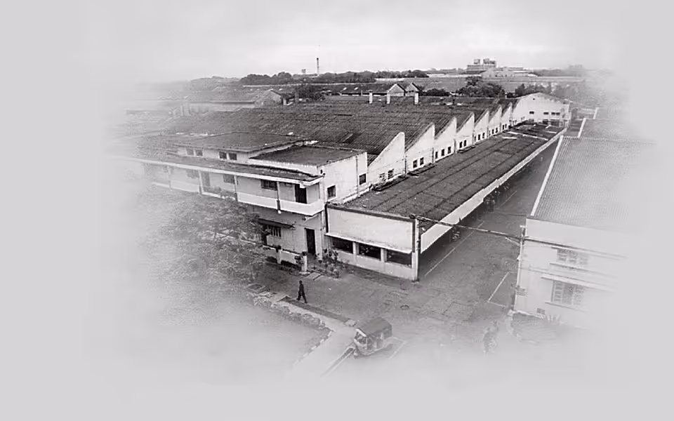Černobílý letecký pohled na průmyslovou budovu a její okolí s osobami a vozíkem v popředí.