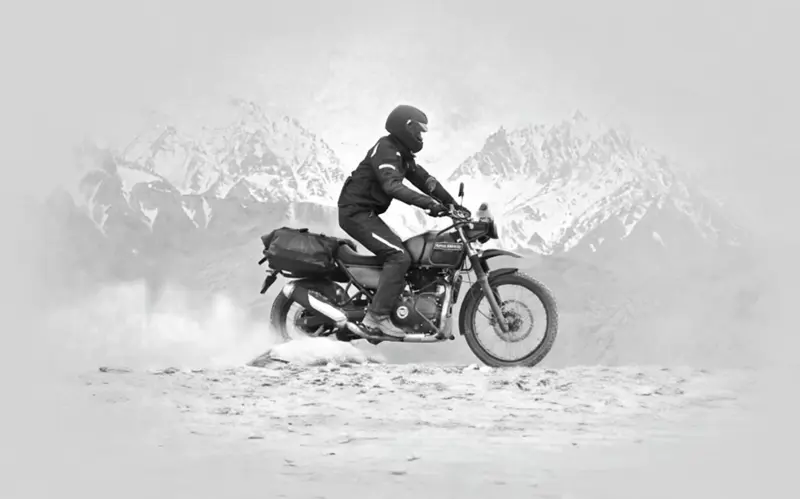 Motocykl Royal Enfield Himalayan na horách s jezdcem v helmě a horským pozadím.